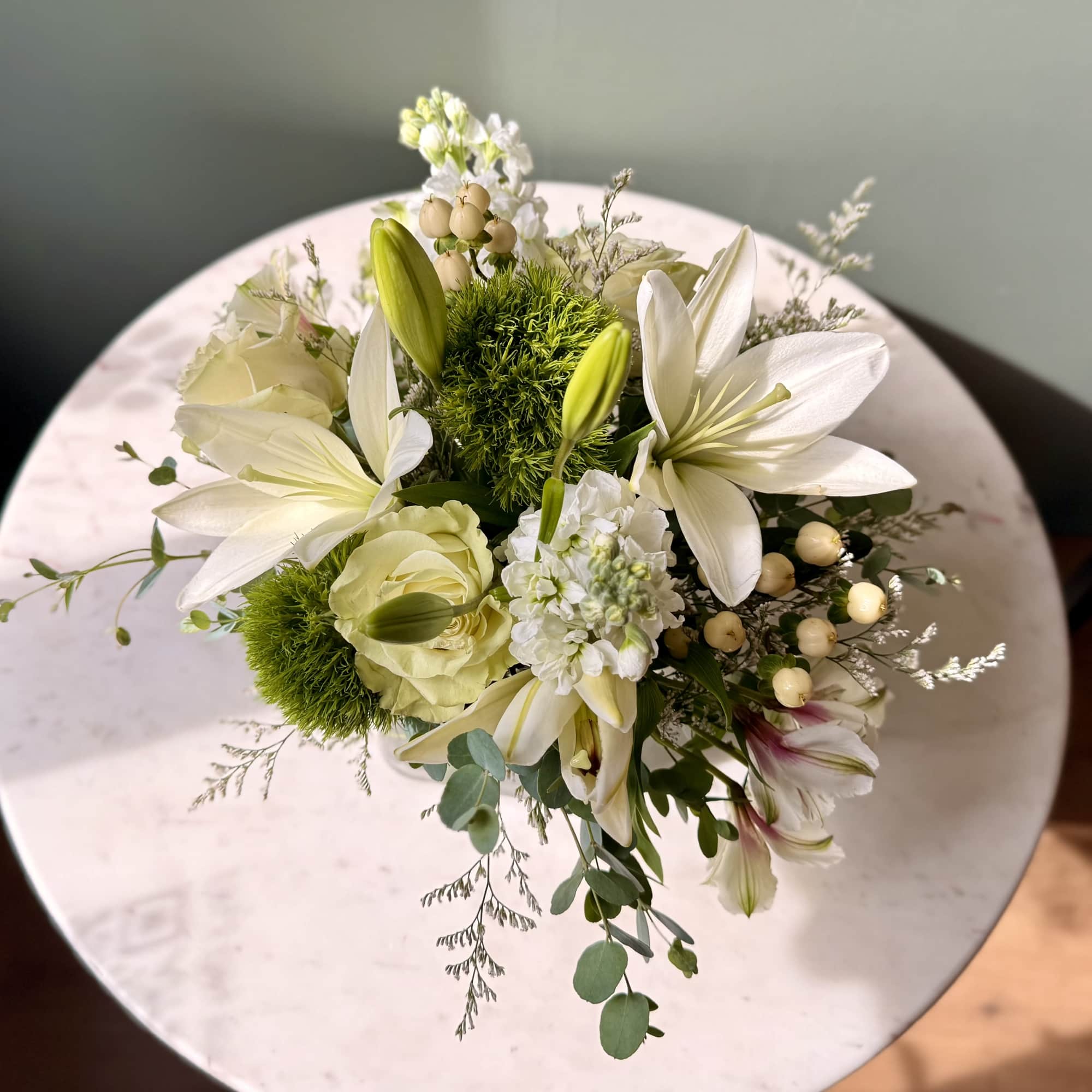 White lily and rose bouquet with green accents on a round table
