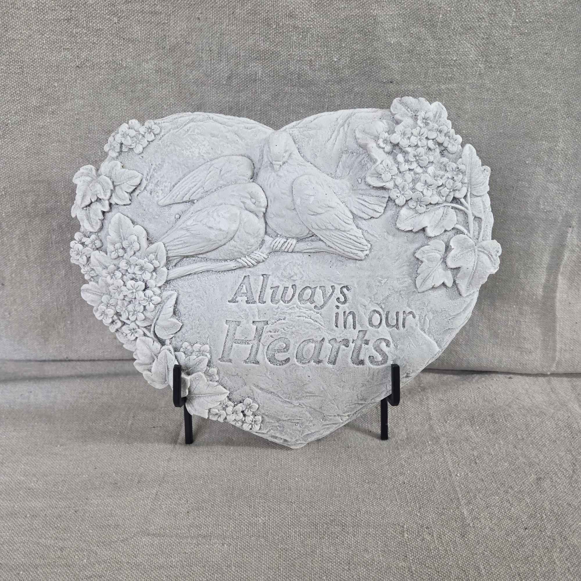Heart-shaped stone memorial plaque with birds, flowers, and 'Always in our Hearts' text