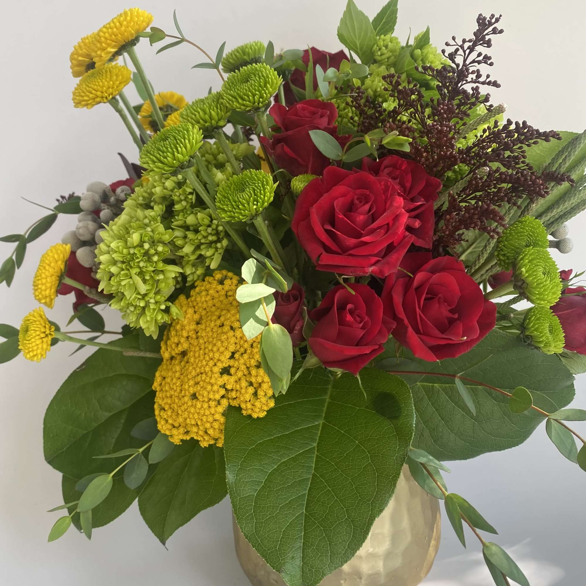 Bouquet of red roses and yellow-green flowers in a gold vase