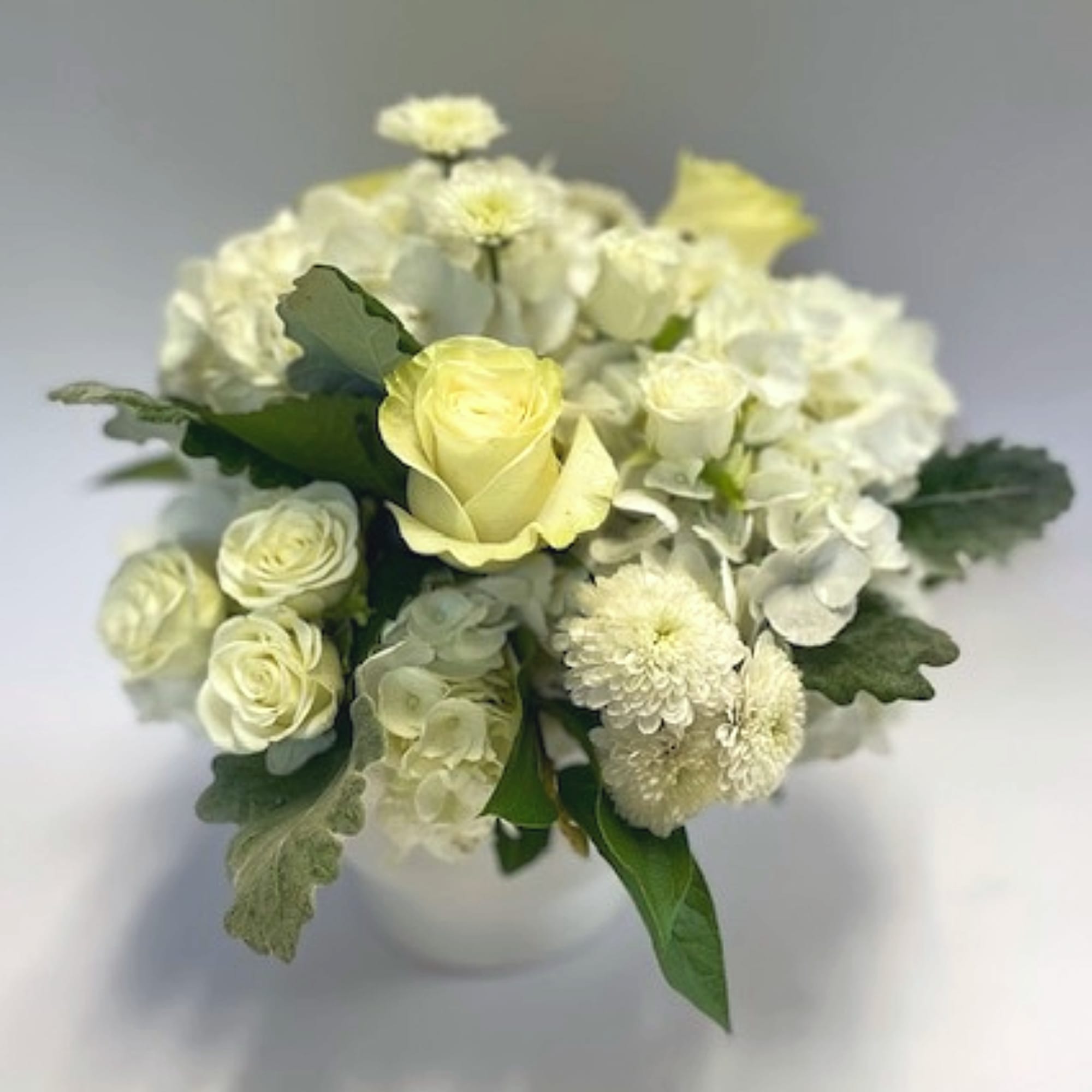 A compact cluster of creamy white hydrangeas, roses, and other seasonal whites