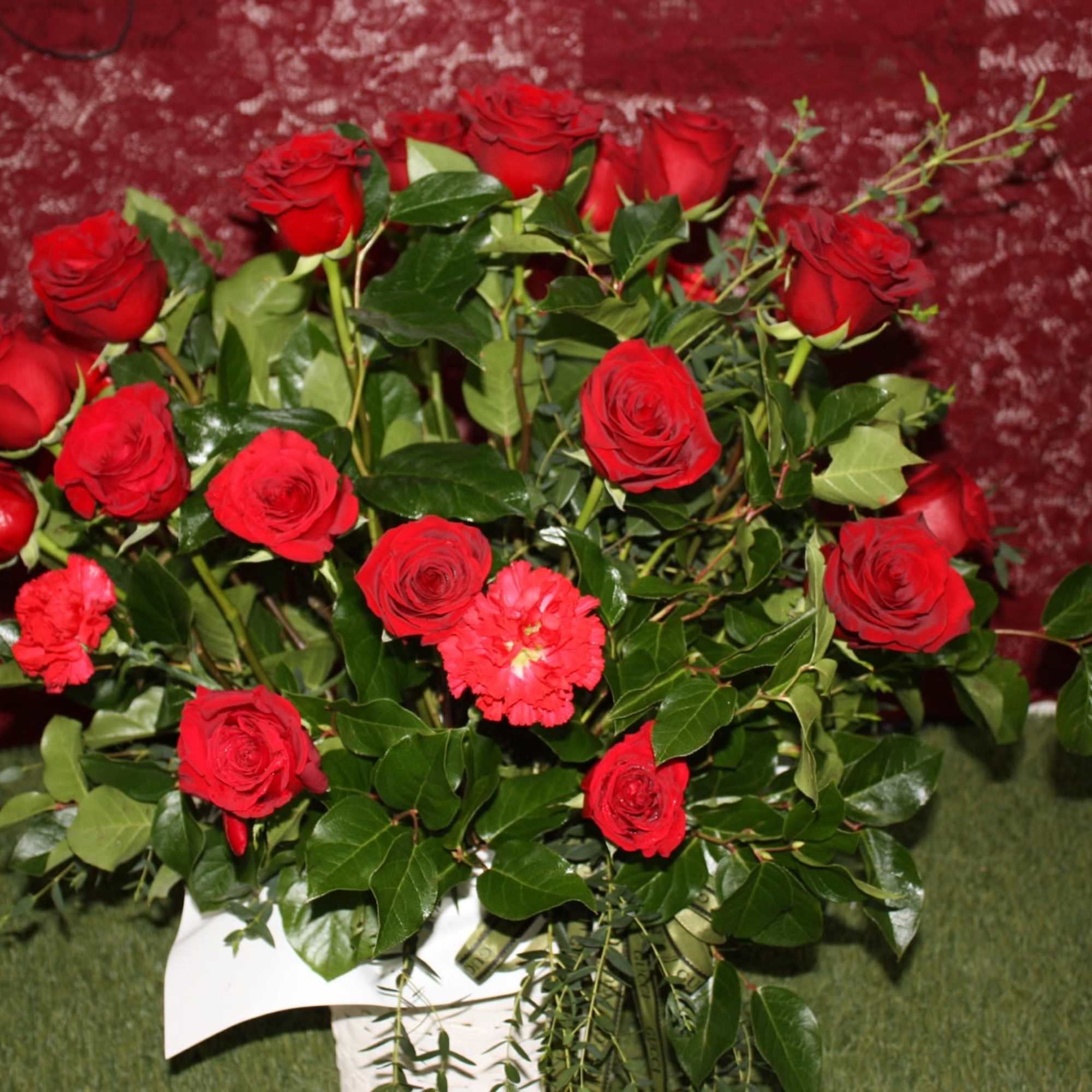 Arrangement of red roses with a few red carnations in a white basket against a burgundy background