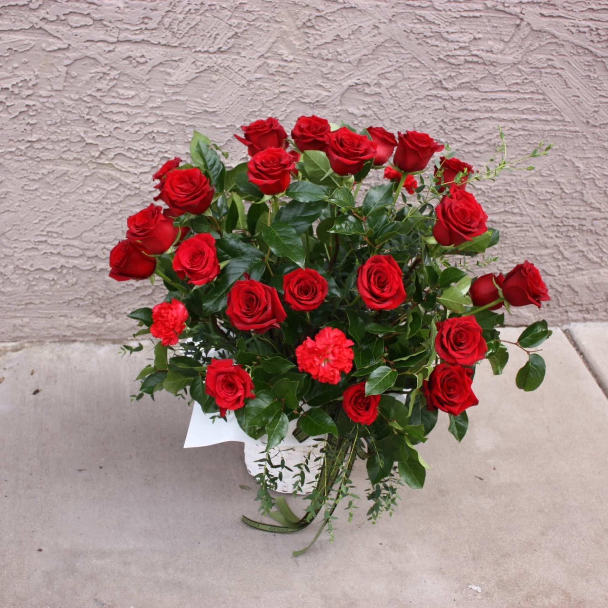 Arrangement of red roses and a few red carnations in a white pot with a small card.