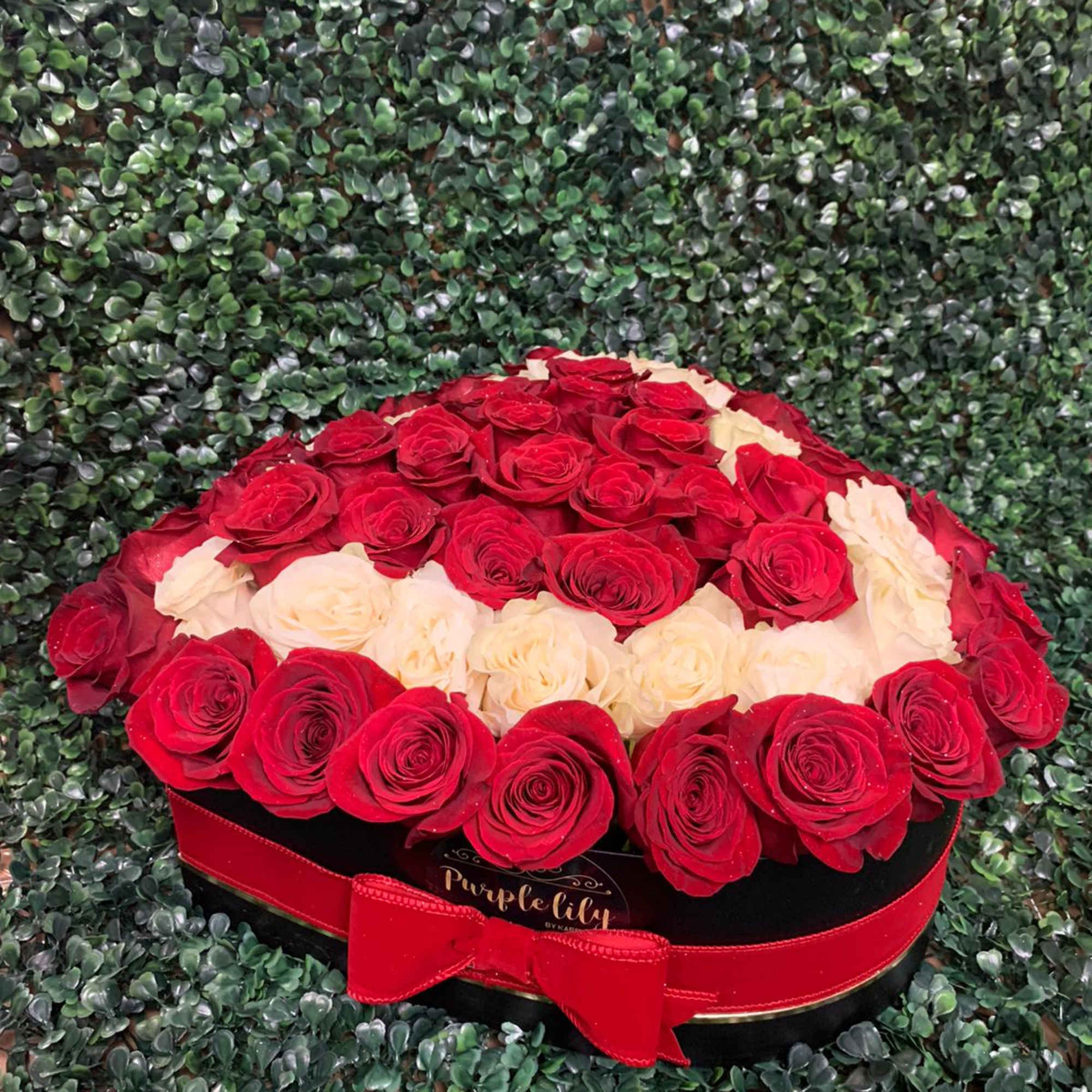 Red and cream roses arranged in a round black box with a red ribbon