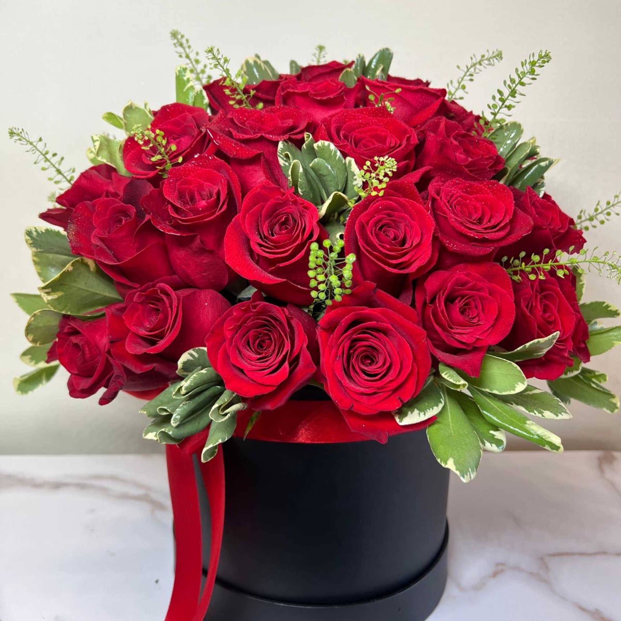 Red roses arranged in a black round box with a red ribbon