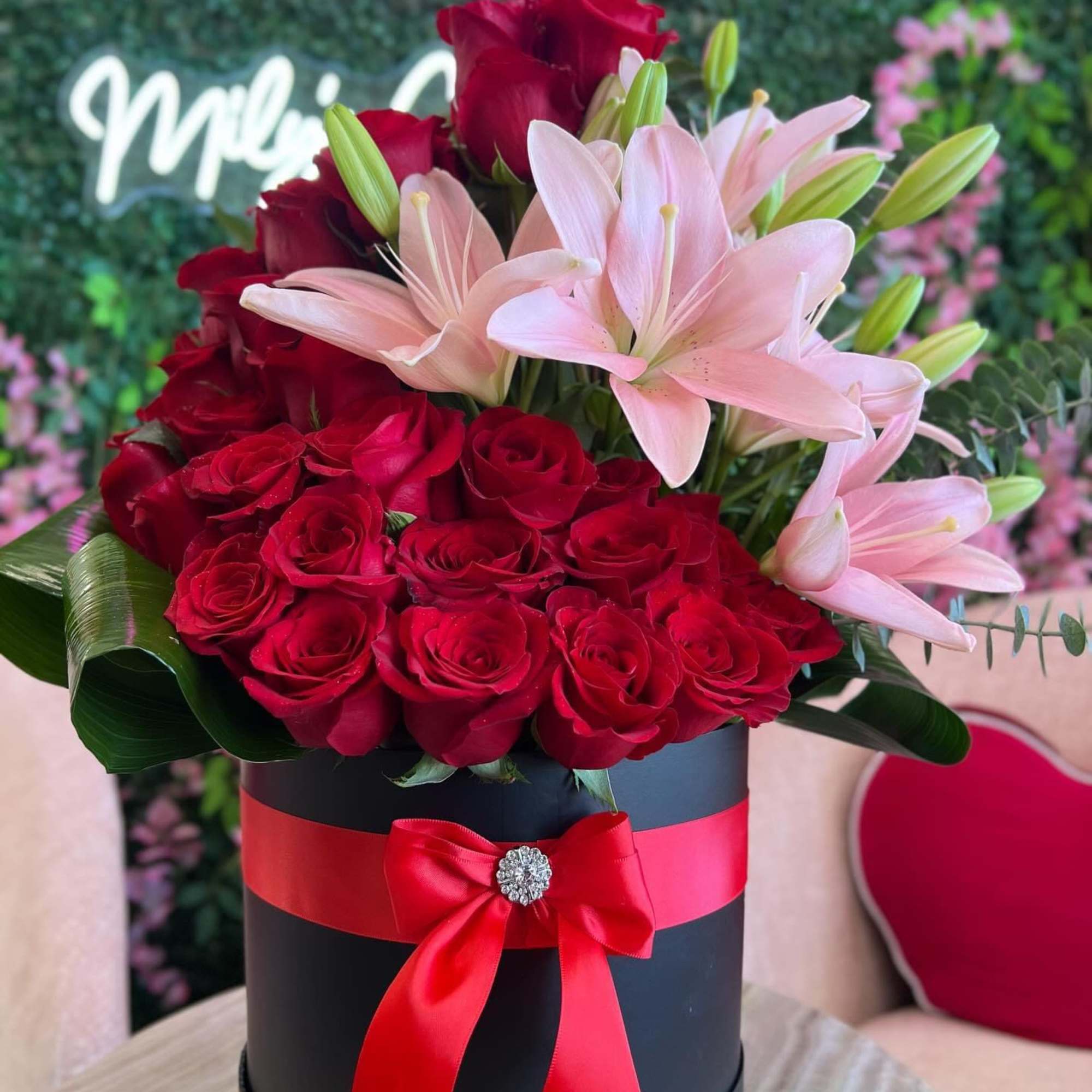 Red roses and pink lilies arranged in a black hat box with a red ribbon.