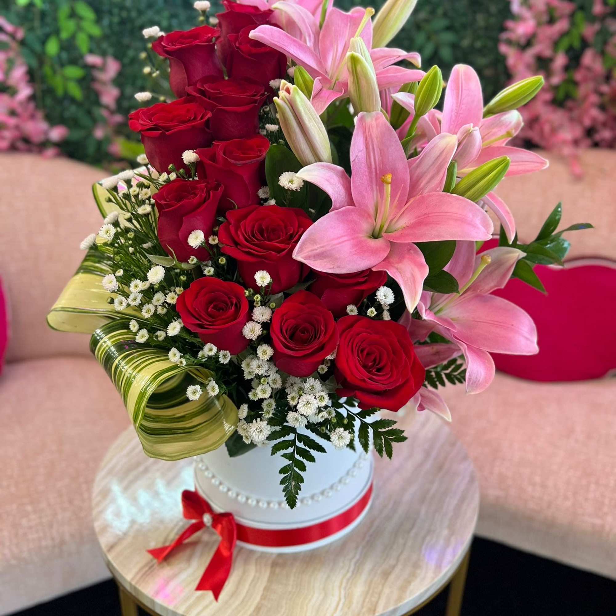 Red roses and pink lilies arranged in a white hatbox with a red ribbon