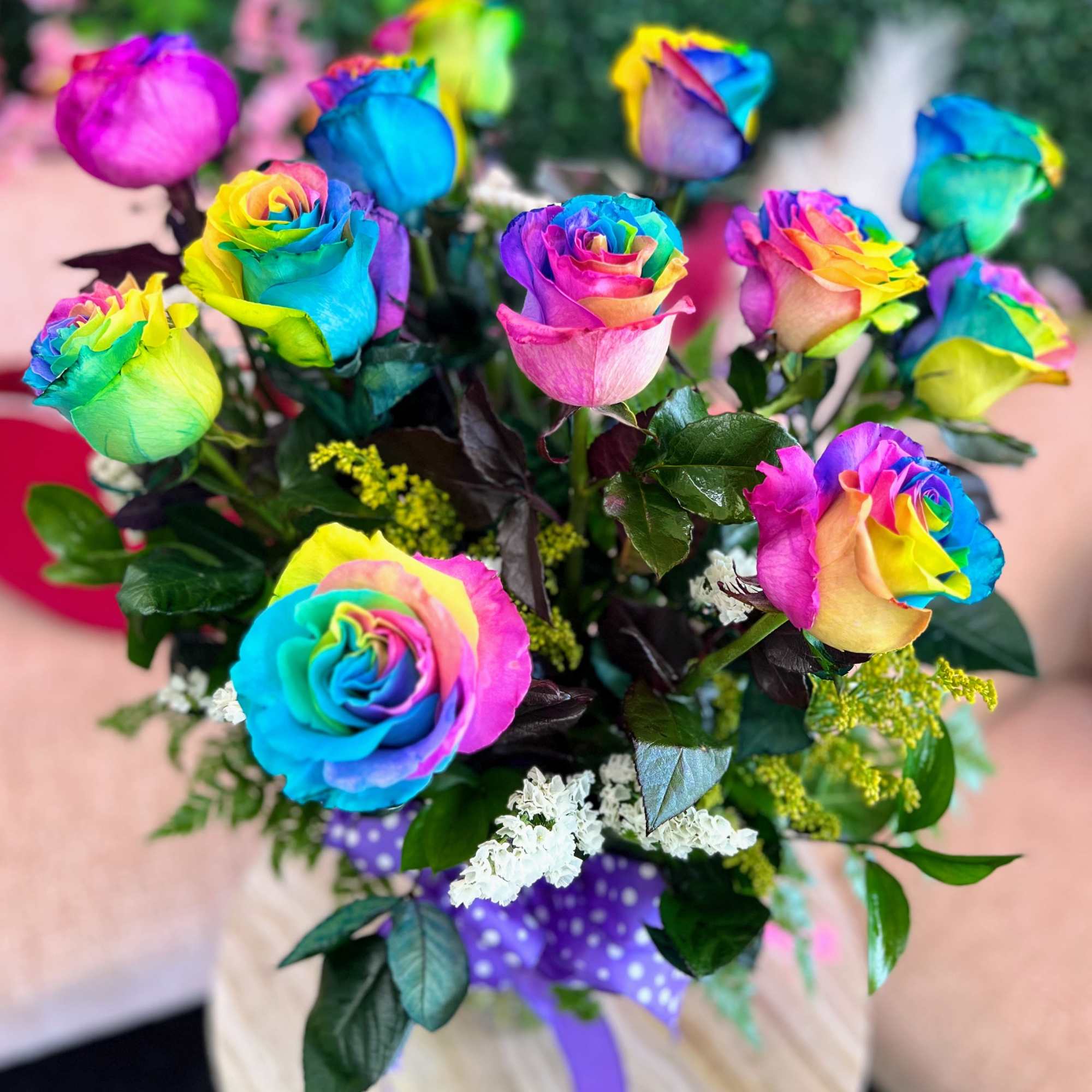 Bouquet of rainbow-colored roses with greenery and a purple polka-dot wrap