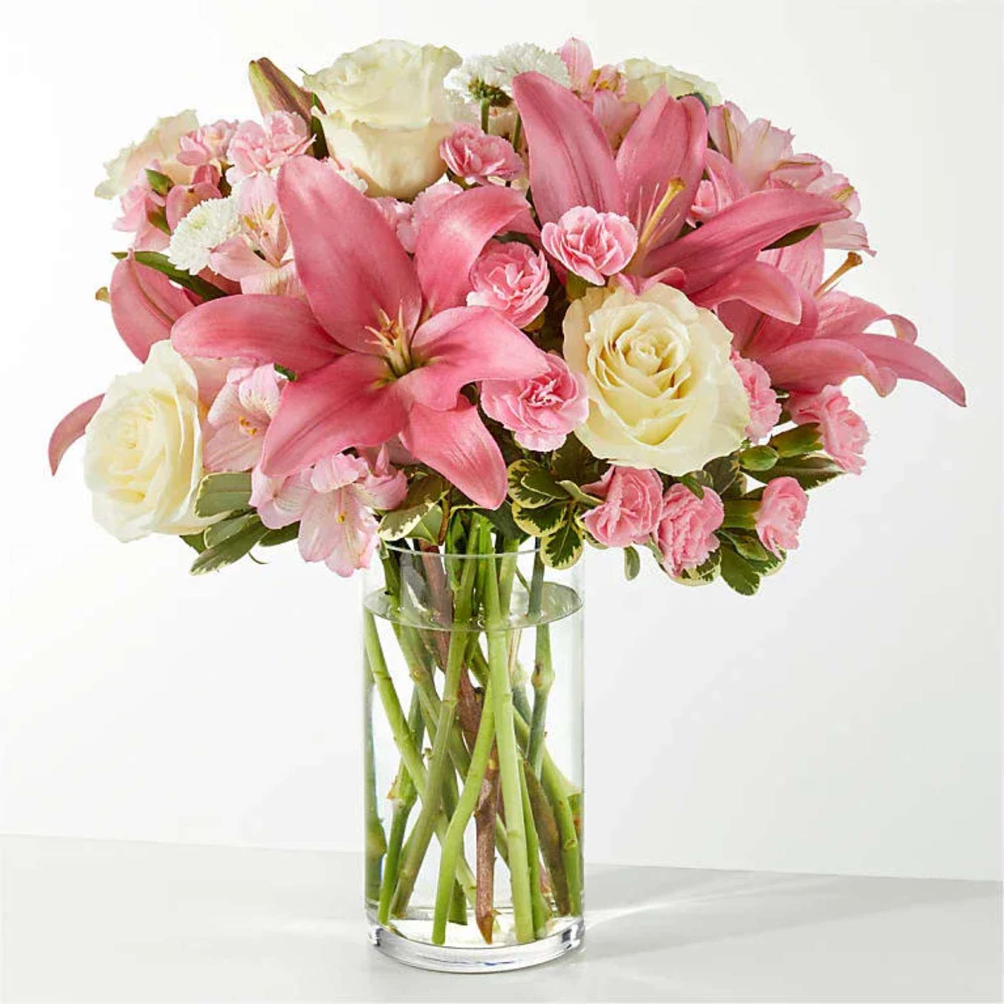 Pink lilies and cream roses arranged in a clear glass vase
