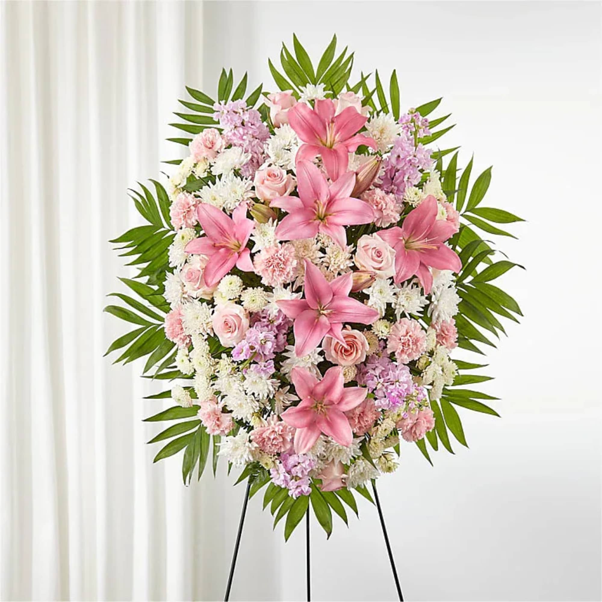 Pink lilies and roses arranged in a standing floral wreath on an easel.