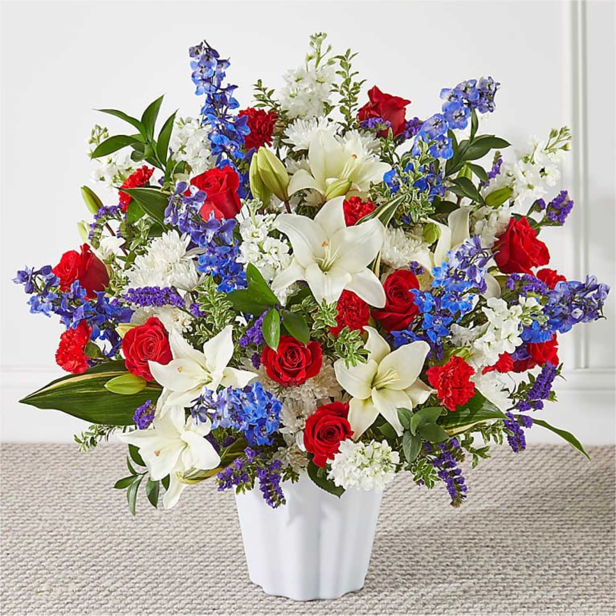 Bouquet of red roses, white lilies, and blue flowers in a white vase