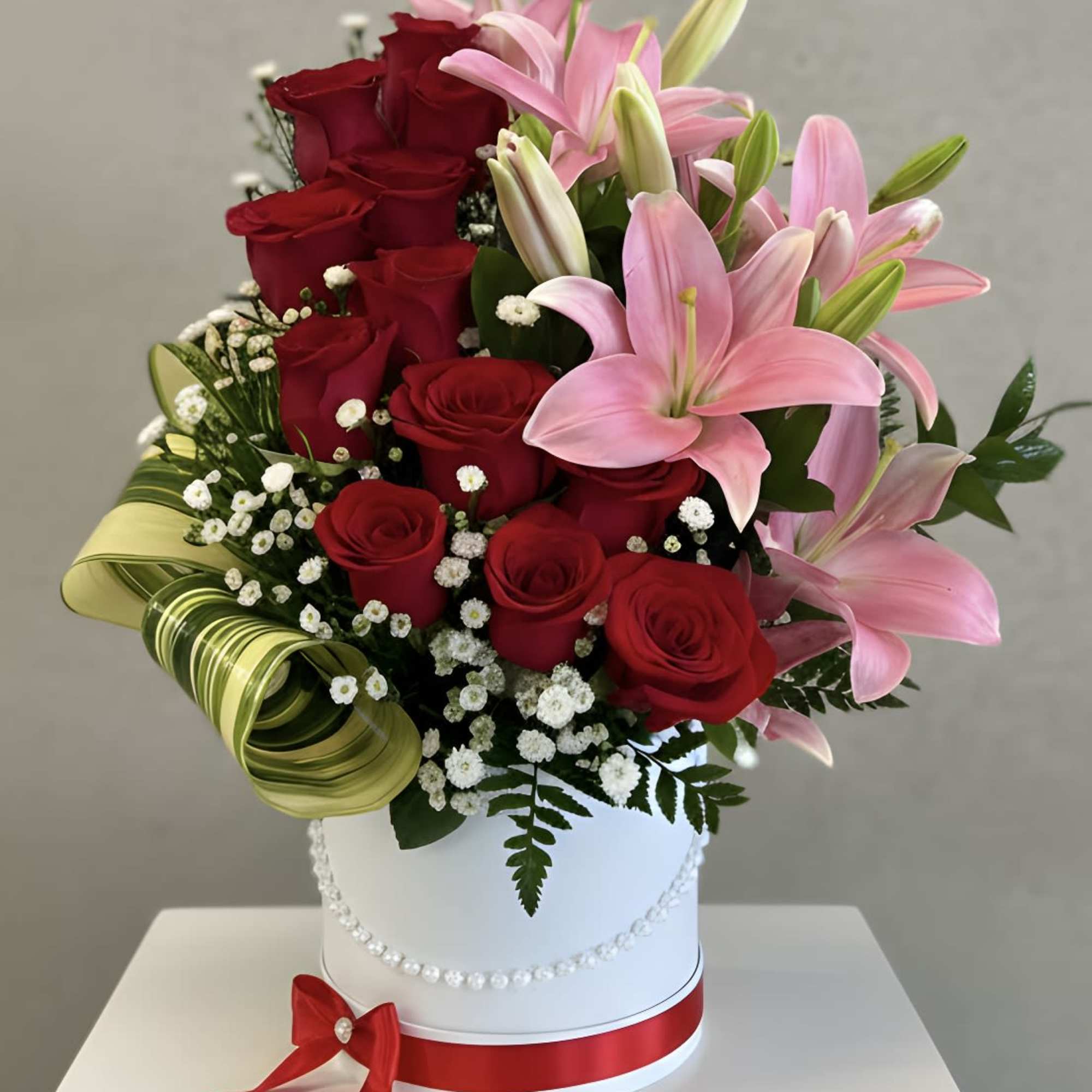 Red roses and pink lilies in a white hatbox with a red ribbon