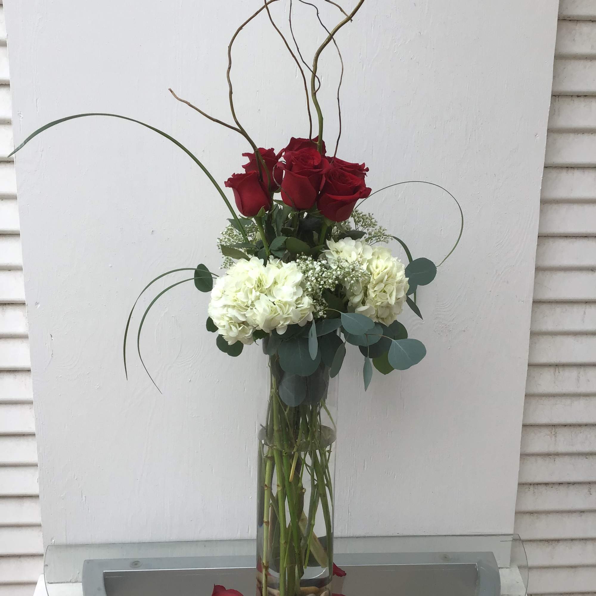 Tall vase arrangement of red roses and white hydrangeas with curly branches