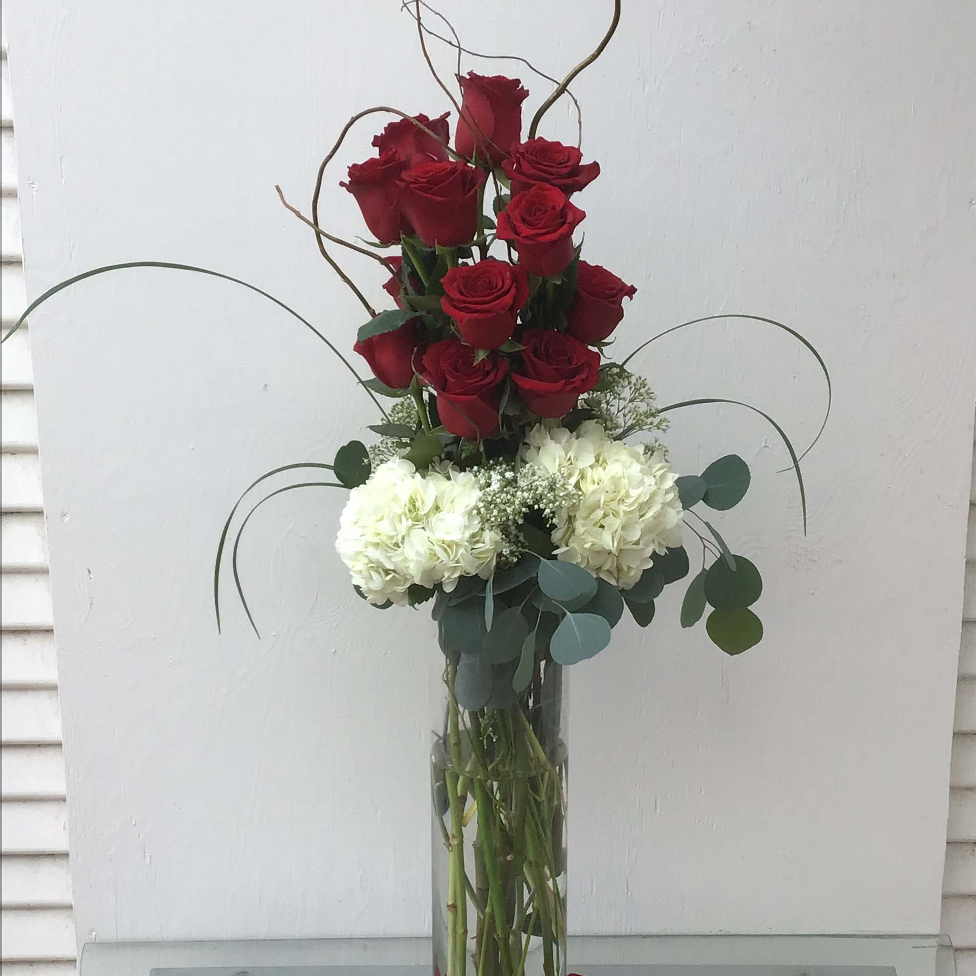 Tall vase arrangement of red roses and white hydrangeas with curly branches