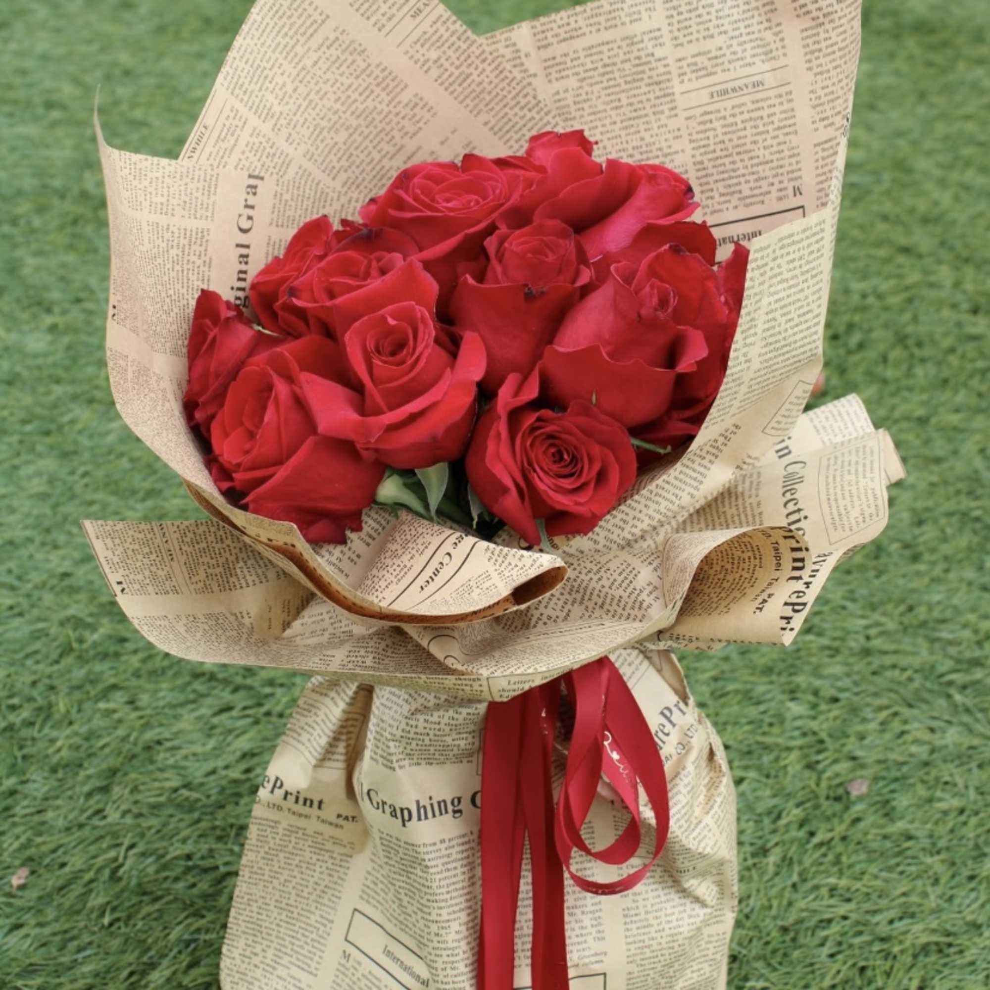 Bouquet of red roses wrapped in newspaper-style paper with a red ribbon, photo 2 of 2