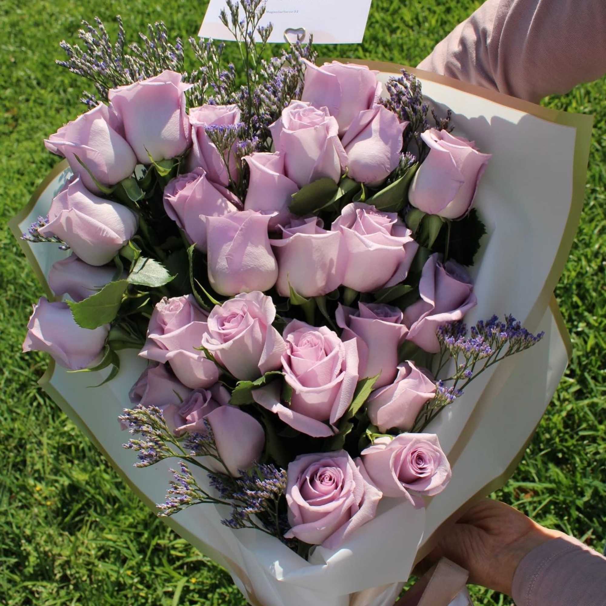 Bouquet of pale pink roses with purple filler flowers wrapped in white paper