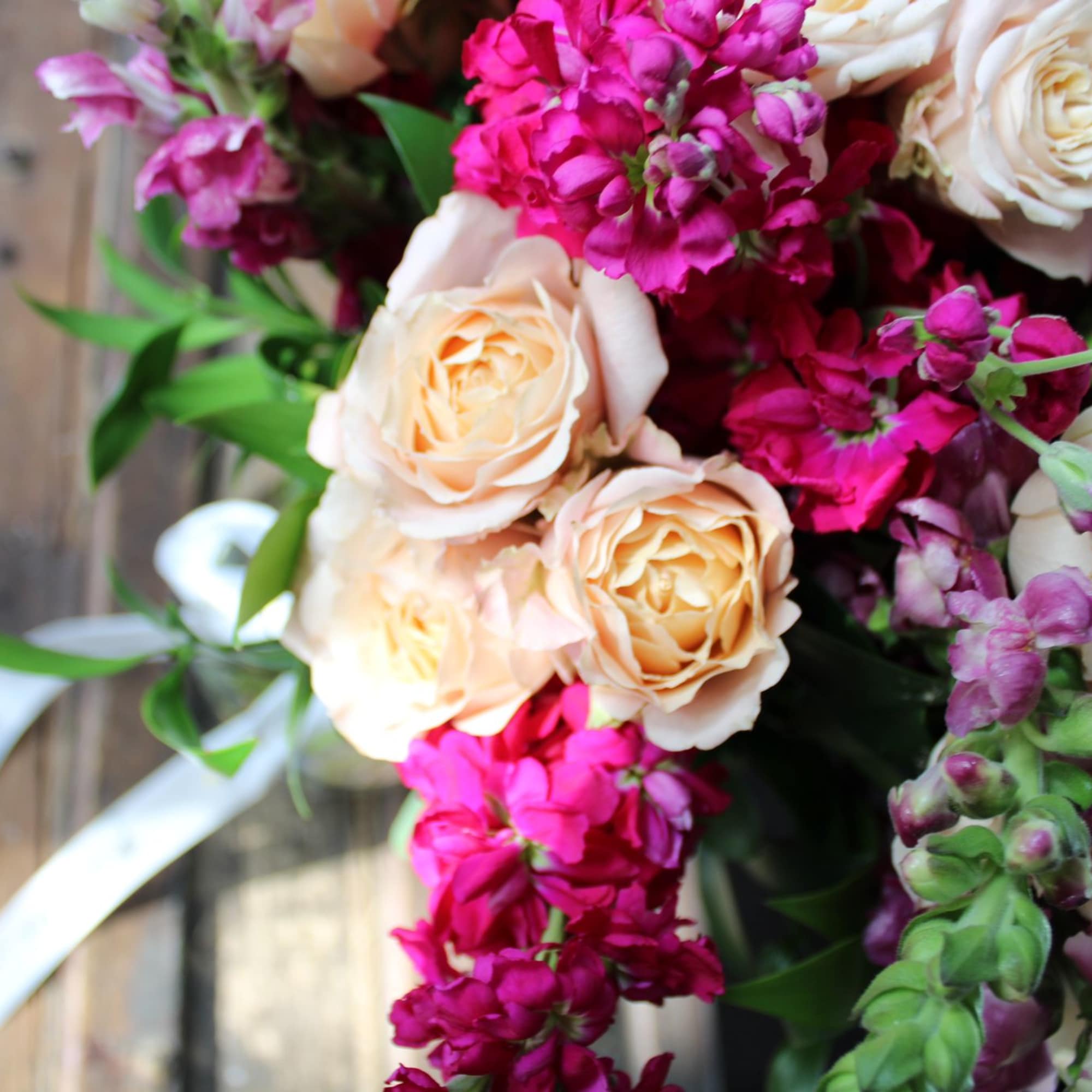 Bouquet of peach roses and magenta flowers with white ribbon