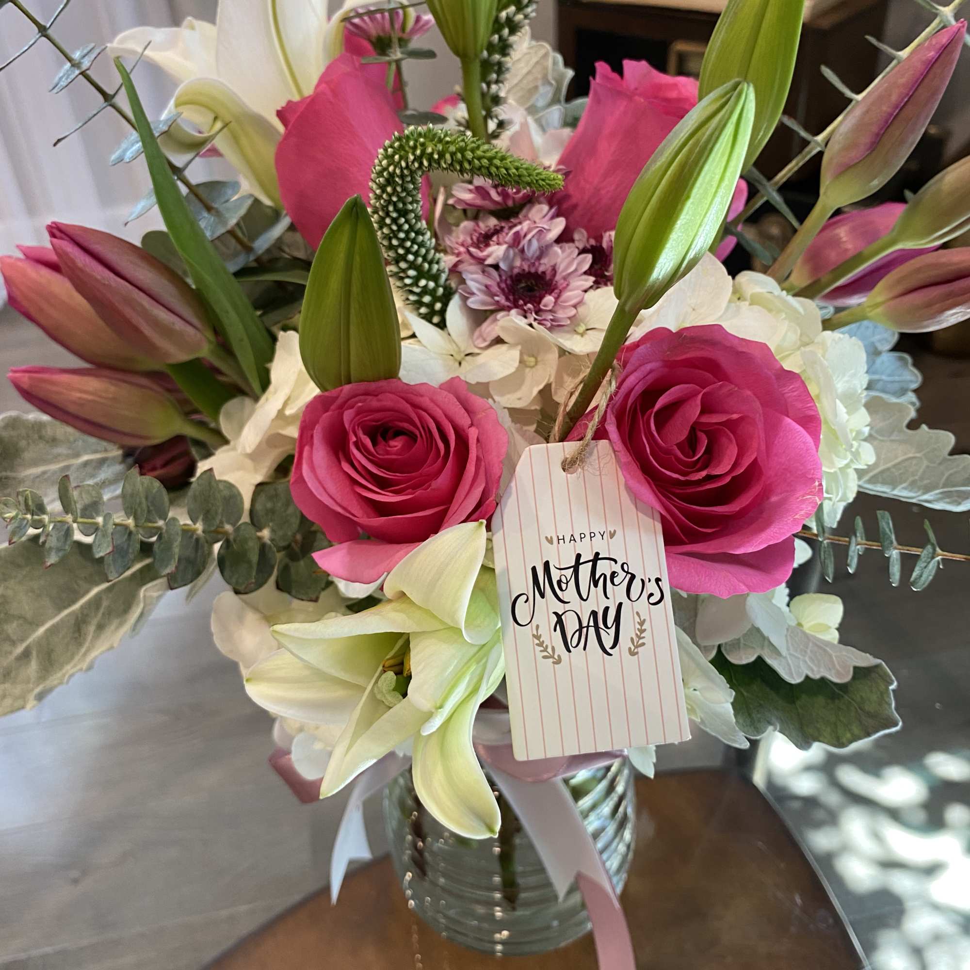 Bouquet of pink roses and white lilies in a glass vase with a Mother's Day tag
