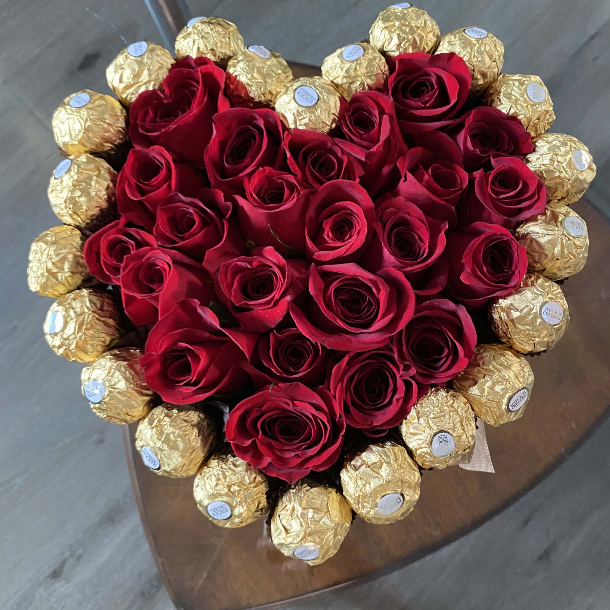 Heart-shaped bouquet of red roses surrounded by gold-wrapped chocolates