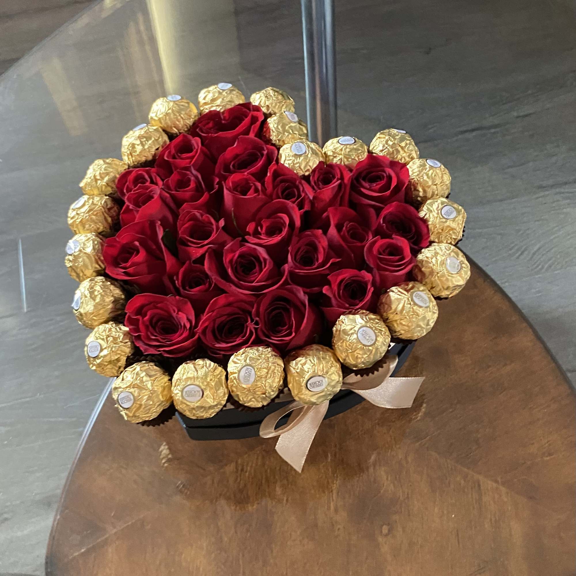 Red roses arranged with gold-wrapped chocolates in a black box