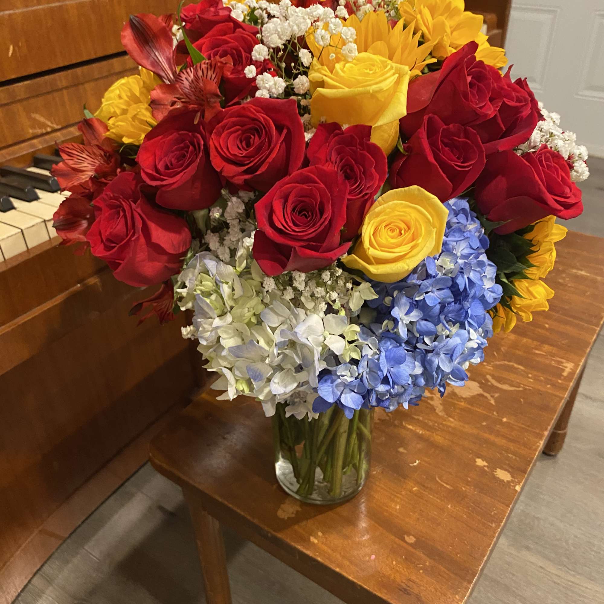 Bouquet of red and yellow roses with blue and white hydrangeas in a glass vase