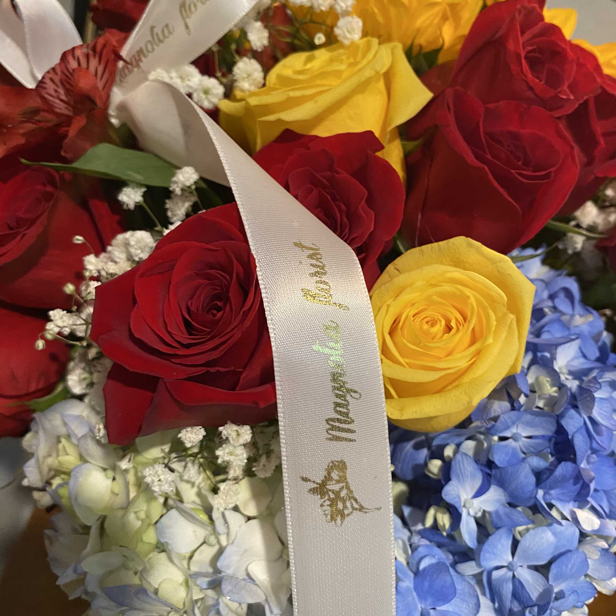 Bouquet of red and yellow roses with blue hydrangeas and white baby's breath