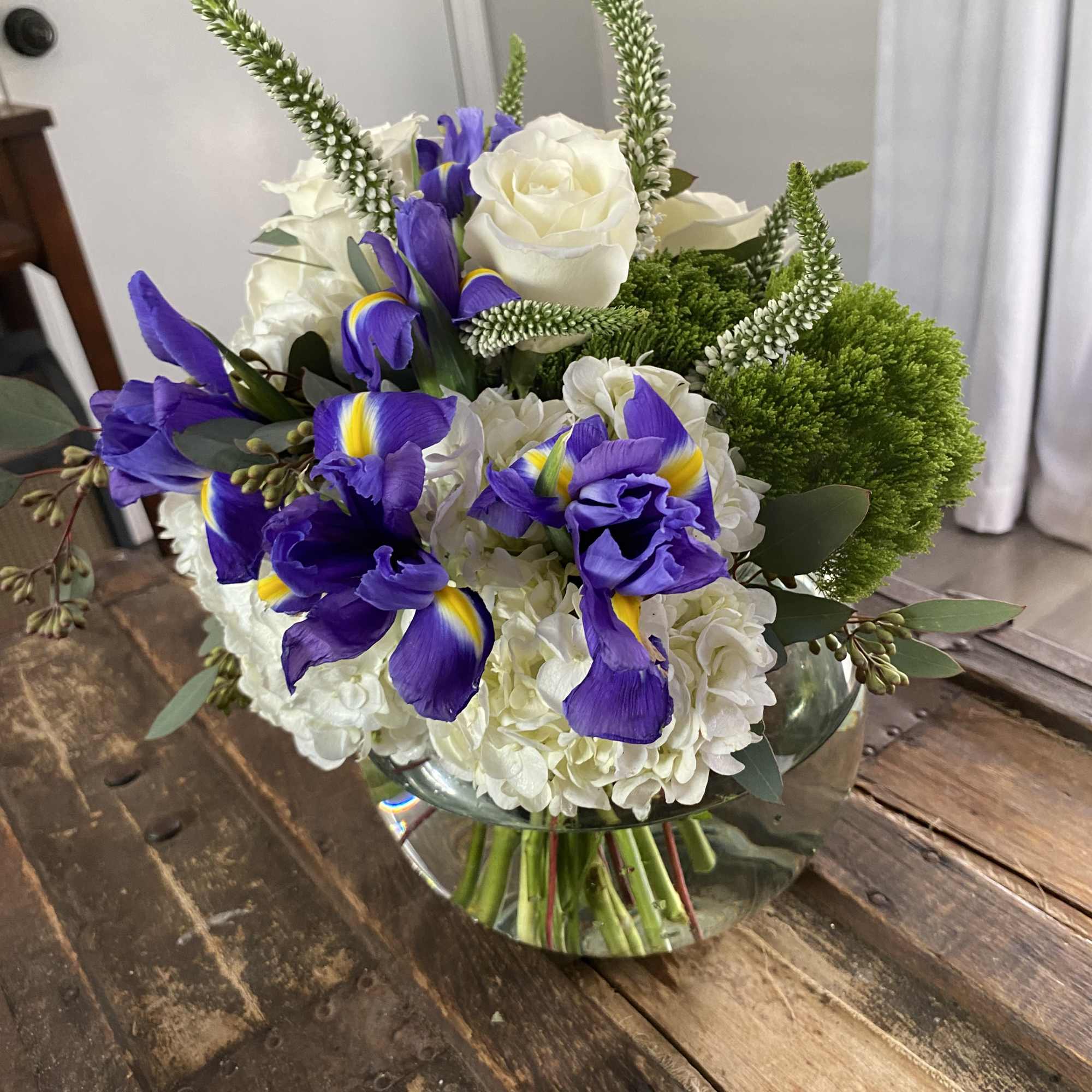 Bouquet of white roses, purple irises, and green accents in a glass vase