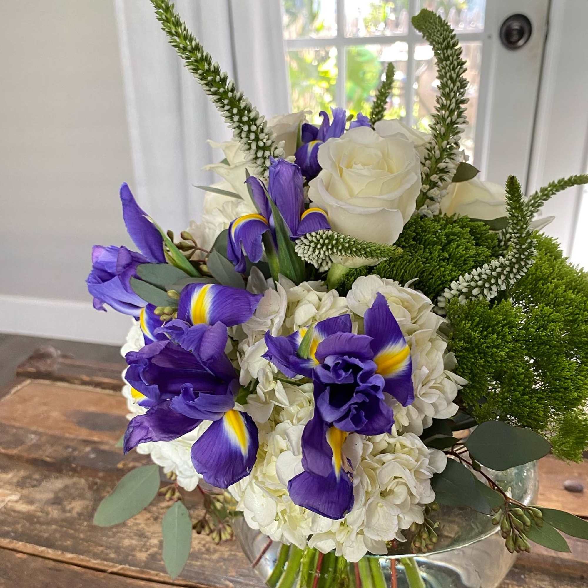 Bouquet of white roses, hydrangeas, and purple irises in a glass vase