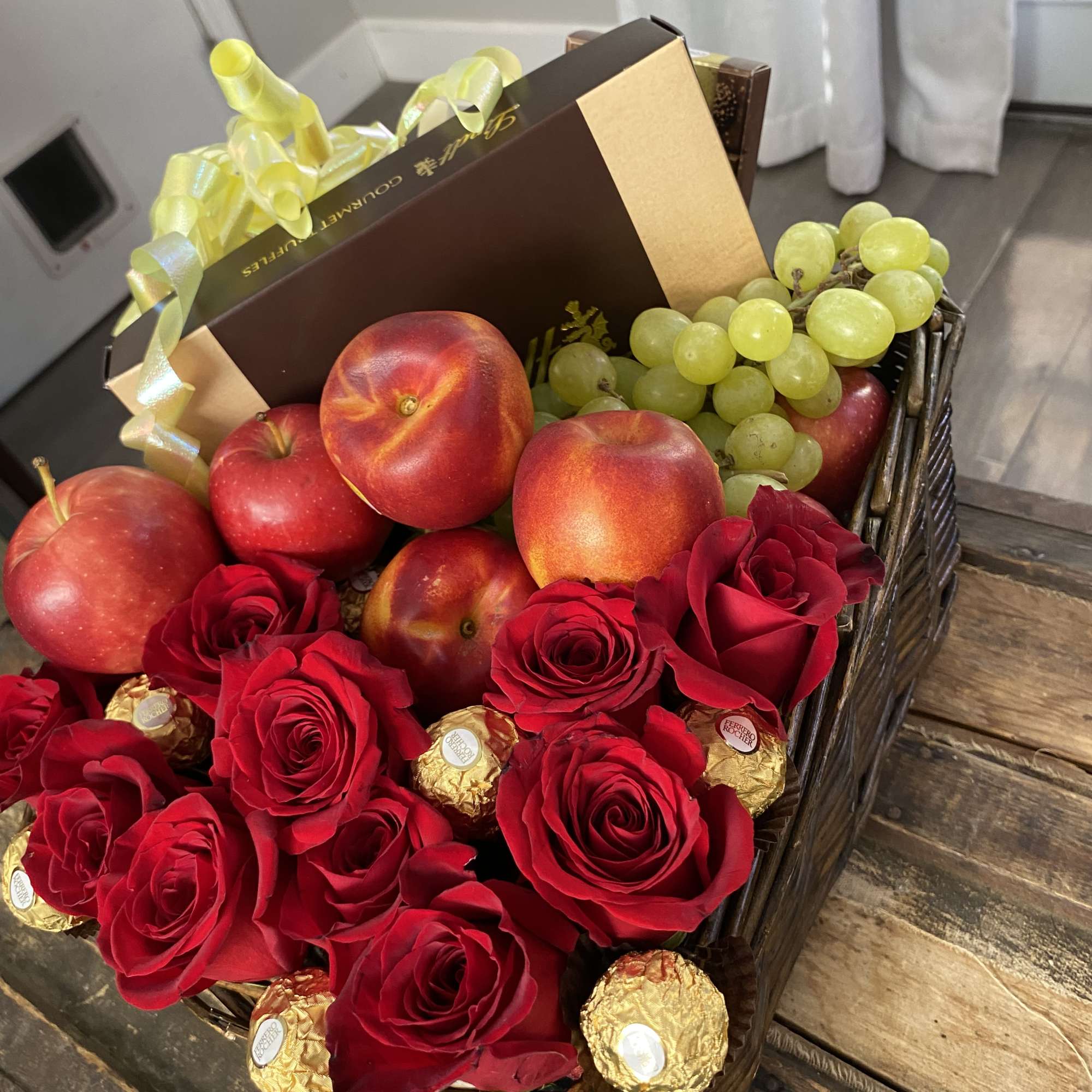 Basket of red roses, fruit, and chocolates with a gift box