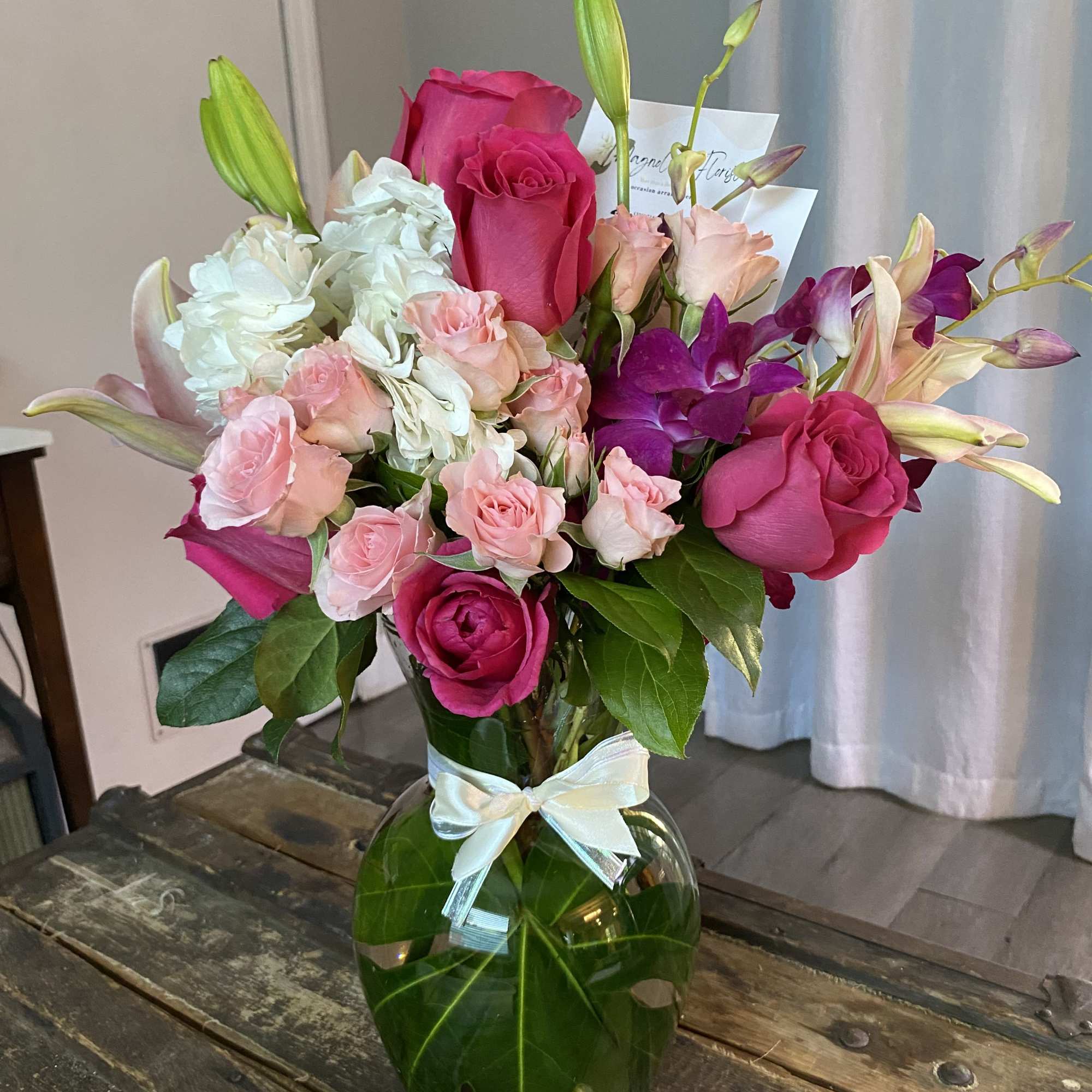 Pink roses and lilies arranged in a glass vase with a ribbon