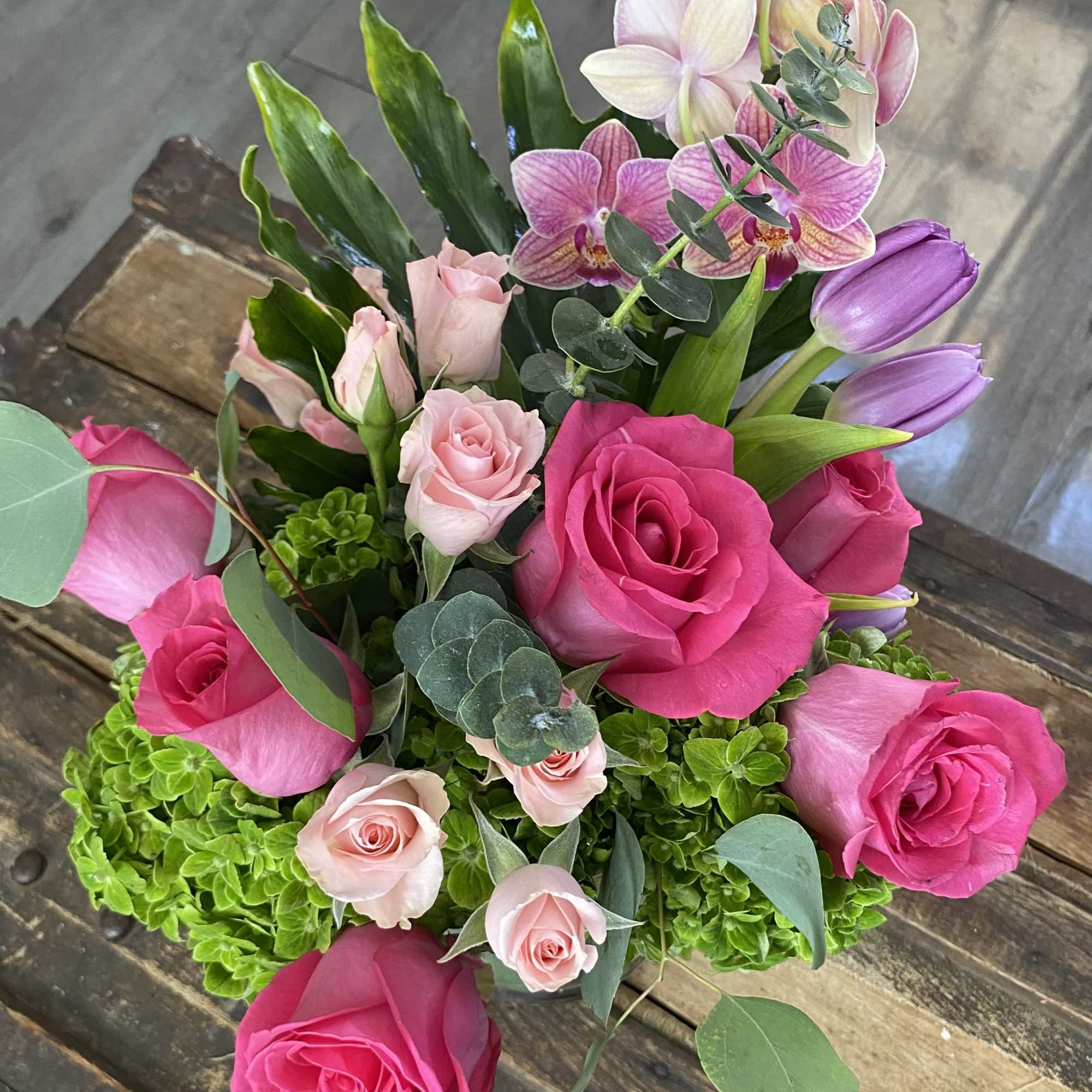 Bouquet of pink roses, tulips, and orchids with green foliage