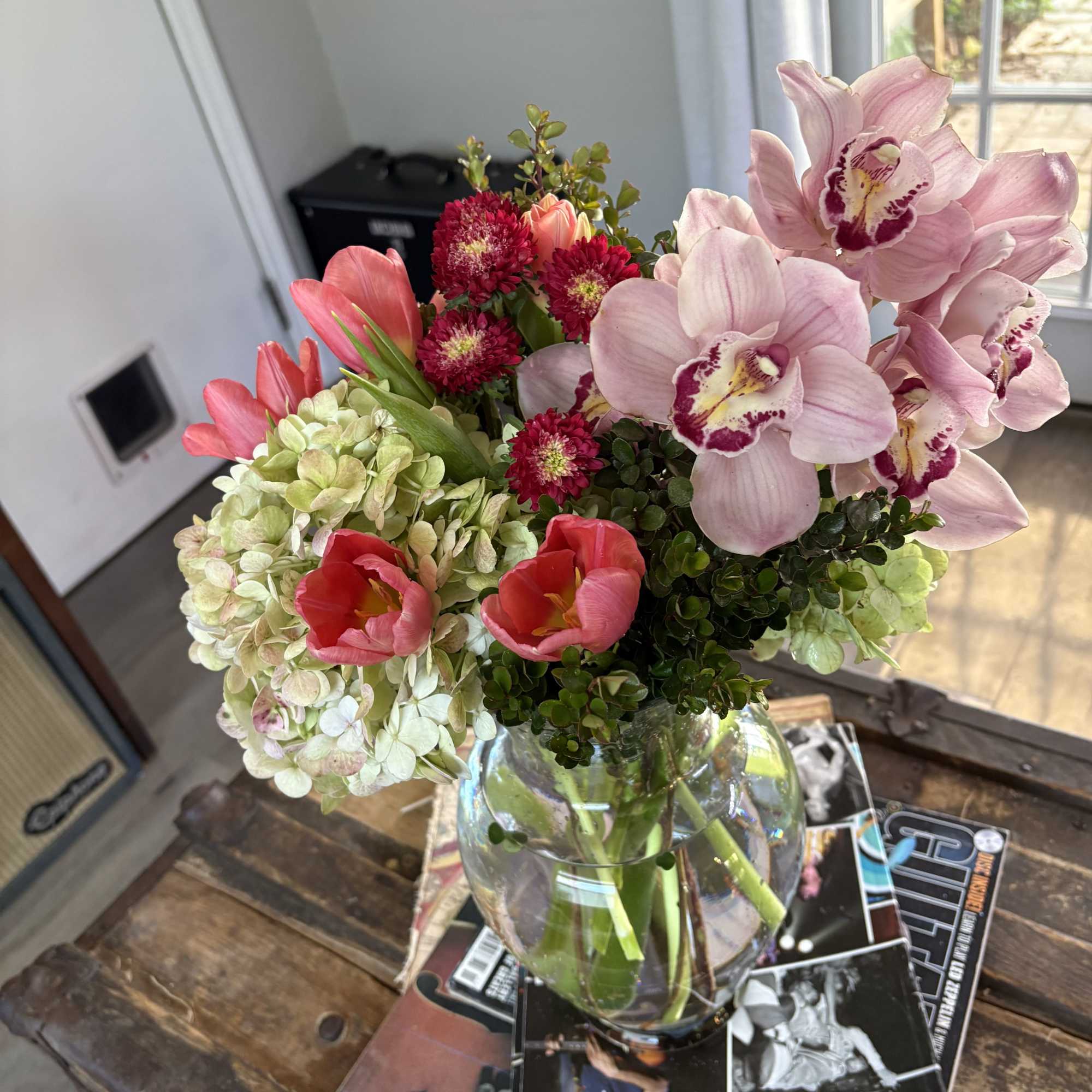 Bouquet of pink orchids, tulips, hydrangeas, and red blooms in a glass vase