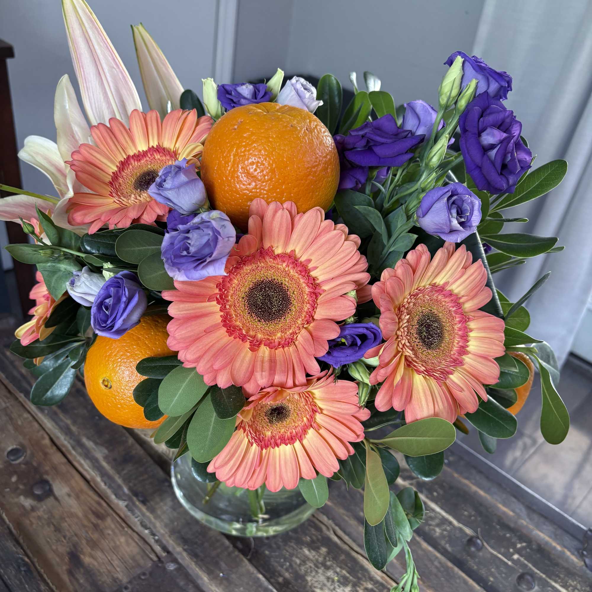 Bouquet of pink gerbera daisies and purple flowers with oranges in a glass vase