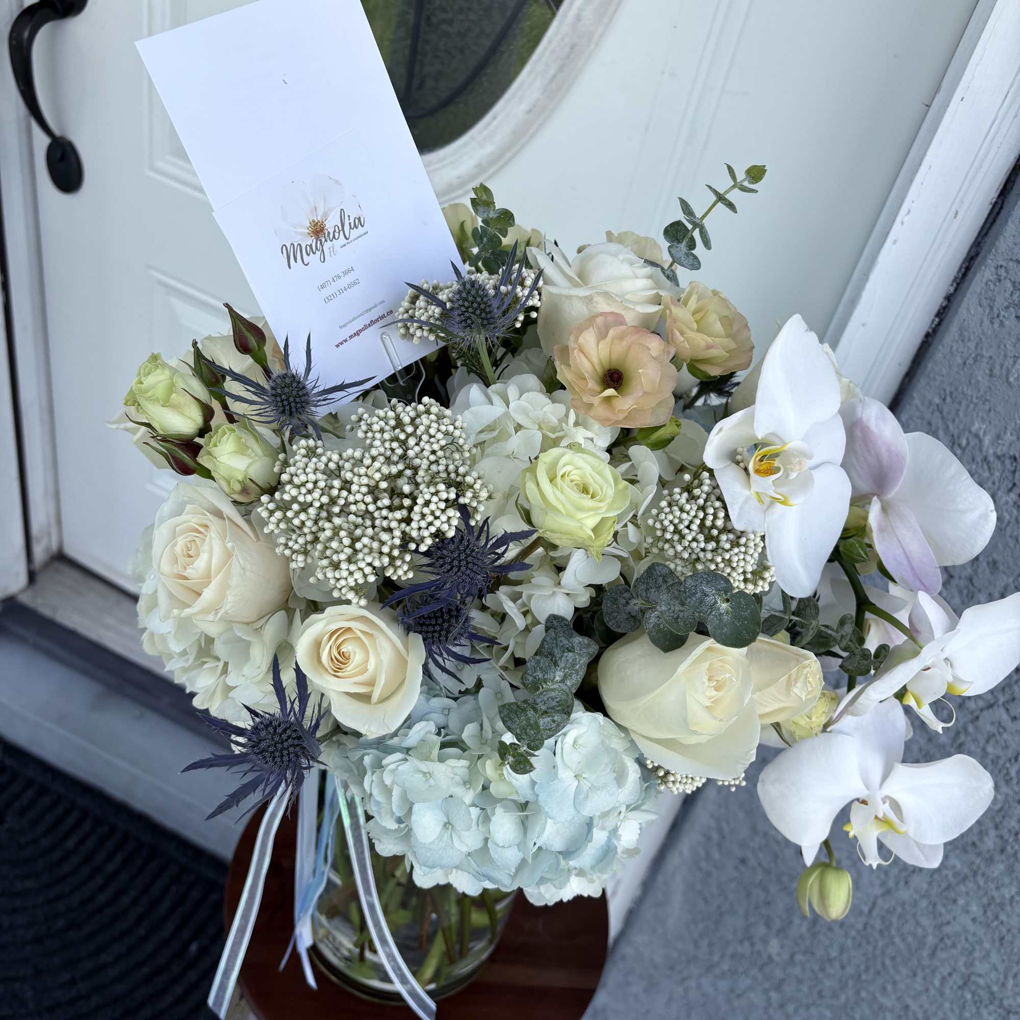 Bouquet of white roses, orchids, and pale hydrangeas in a glass vase
