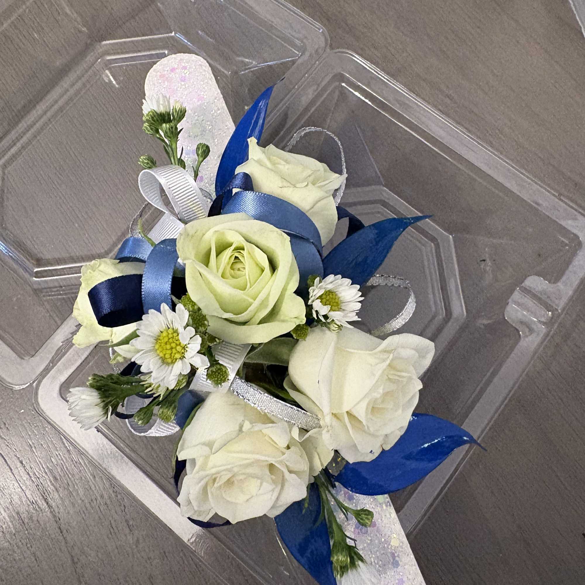 Small corsage with white roses and daisies on a clear plastic tray