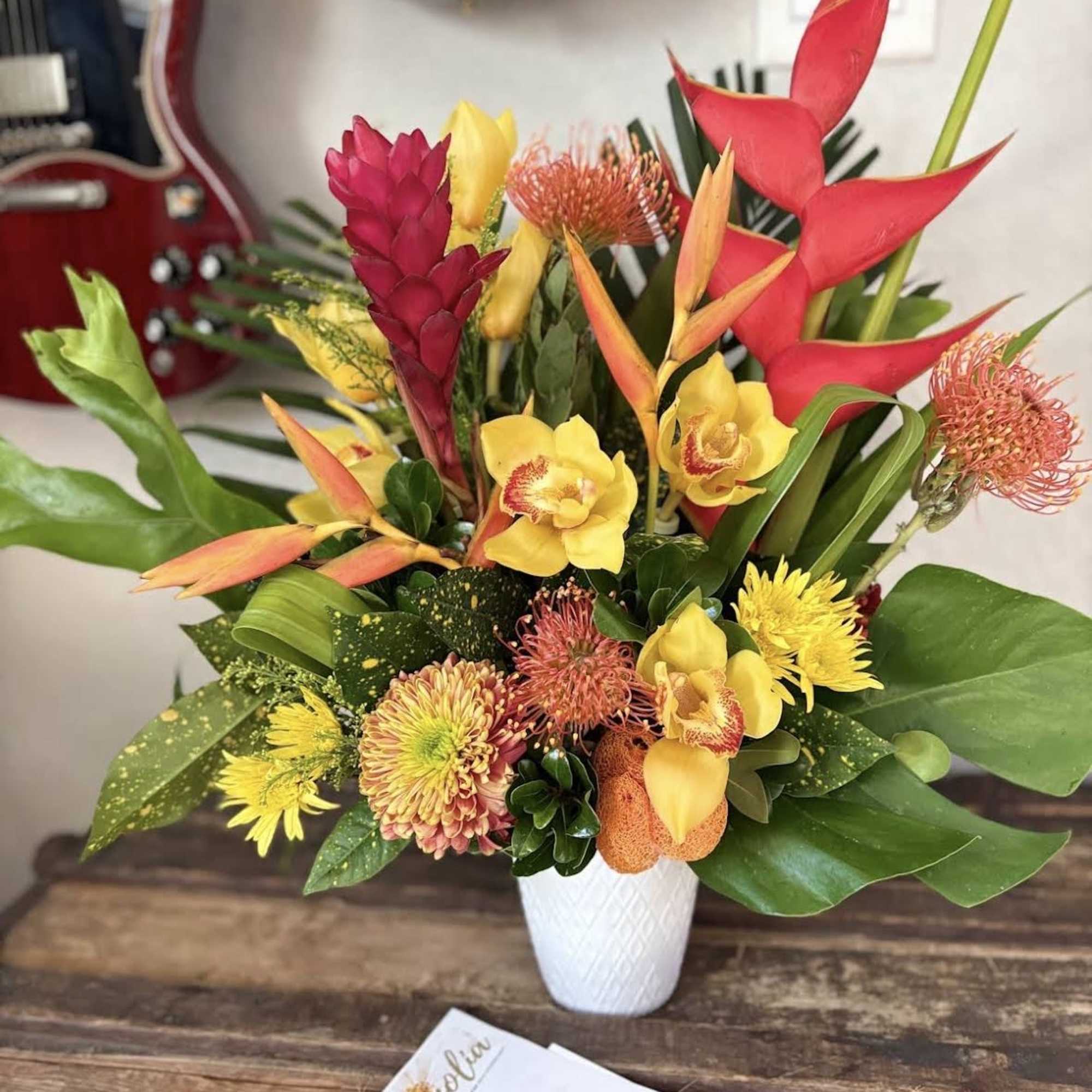 Tropical bouquet with red heliconia and yellow orchids in a white vase
