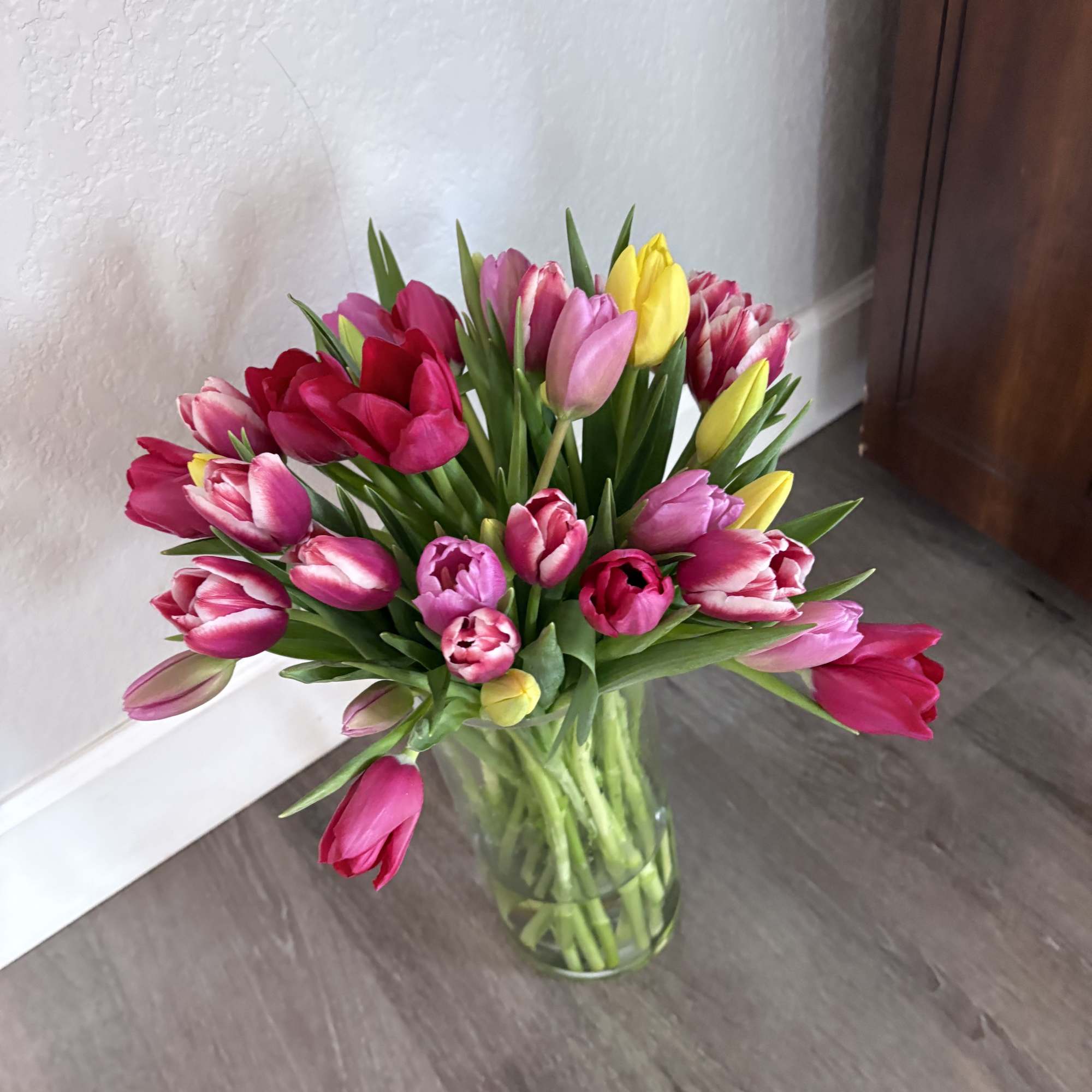 Bouquet of pink, red, and yellow tulips in a clear glass vase, photo 2 of 2