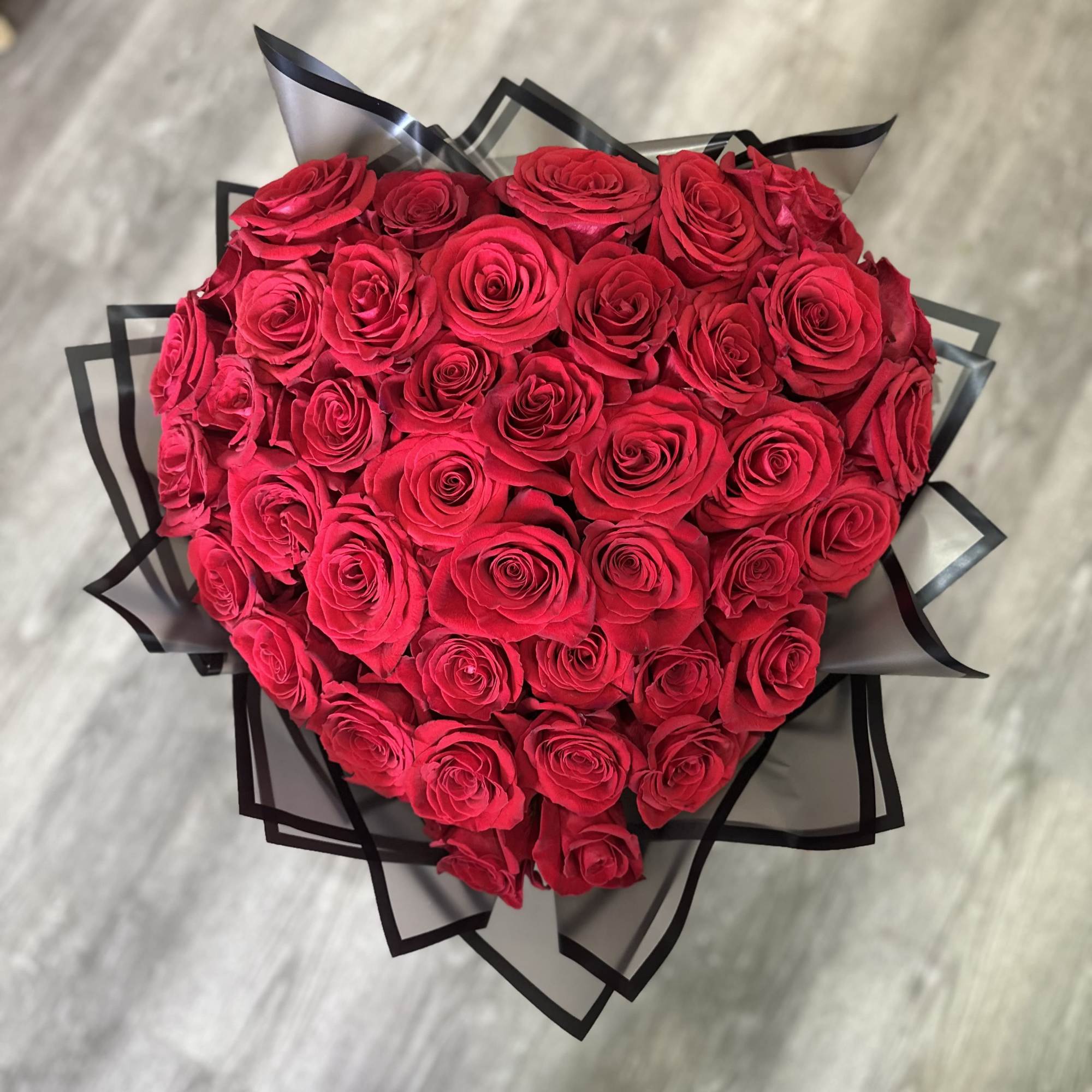 Heart-shaped bouquet of red roses wrapped in black and clear paper