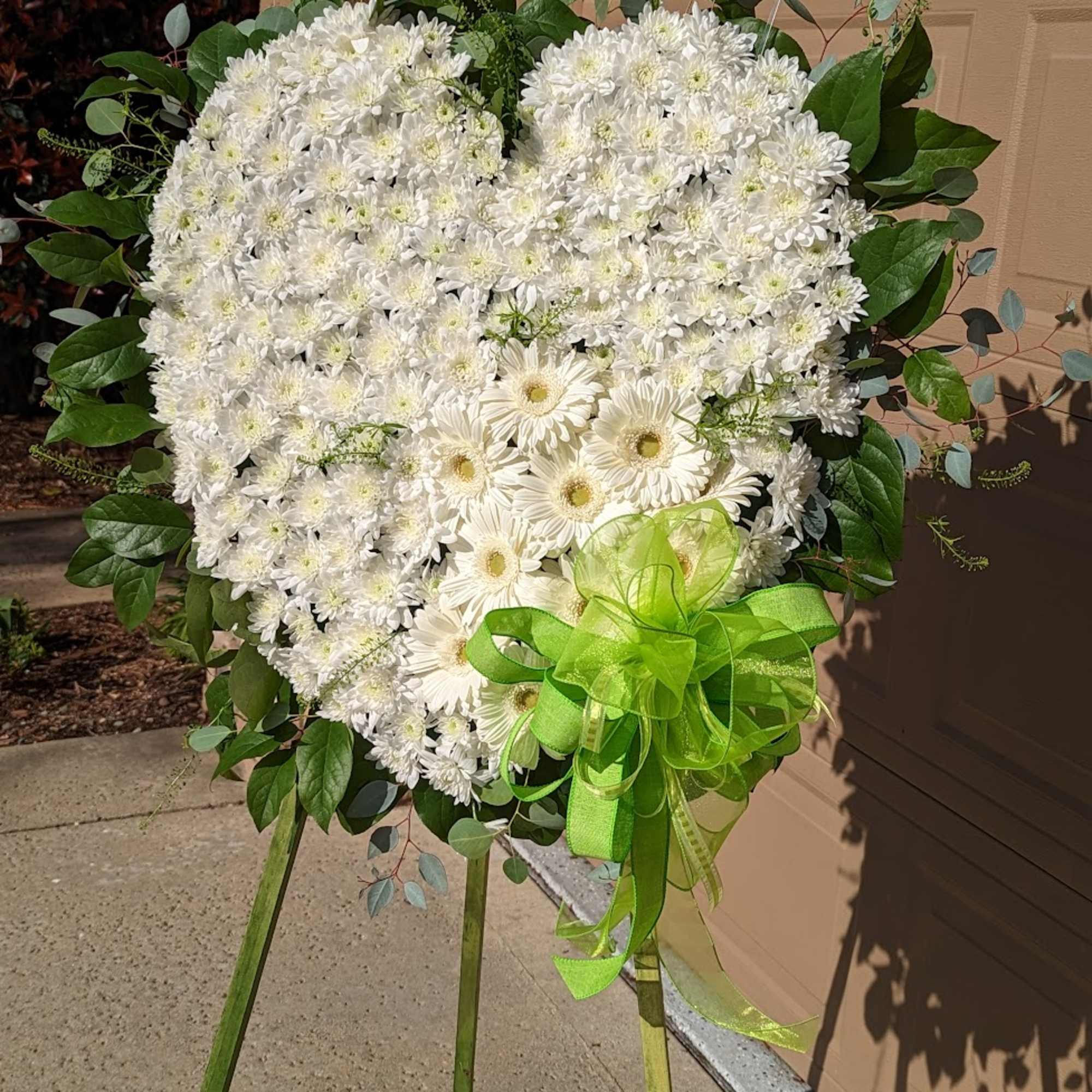 Heart-shaped white floral standing spray with a green ribbon bow