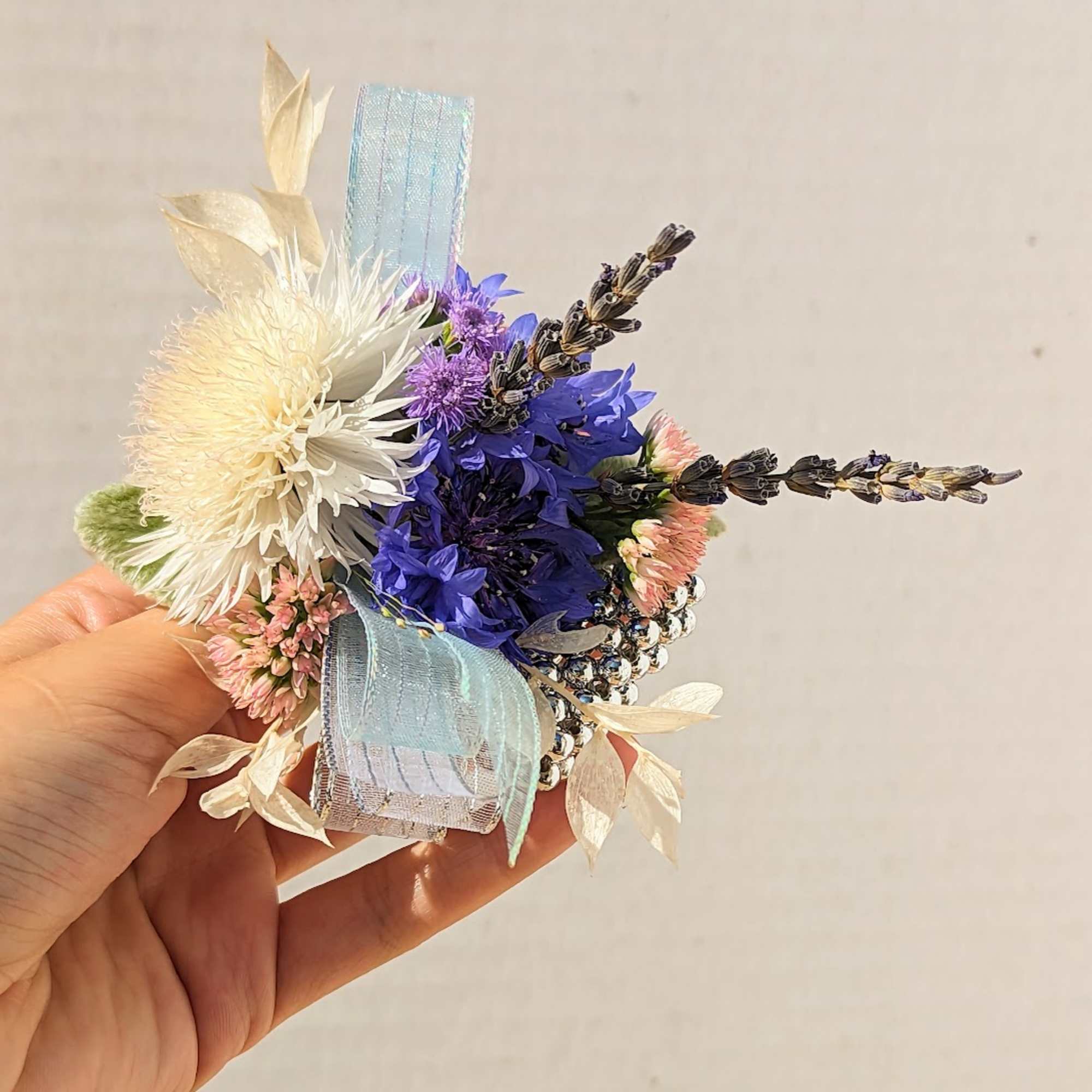 Small hand-held floral corsage with blue, white, and pink flowers and ribbon