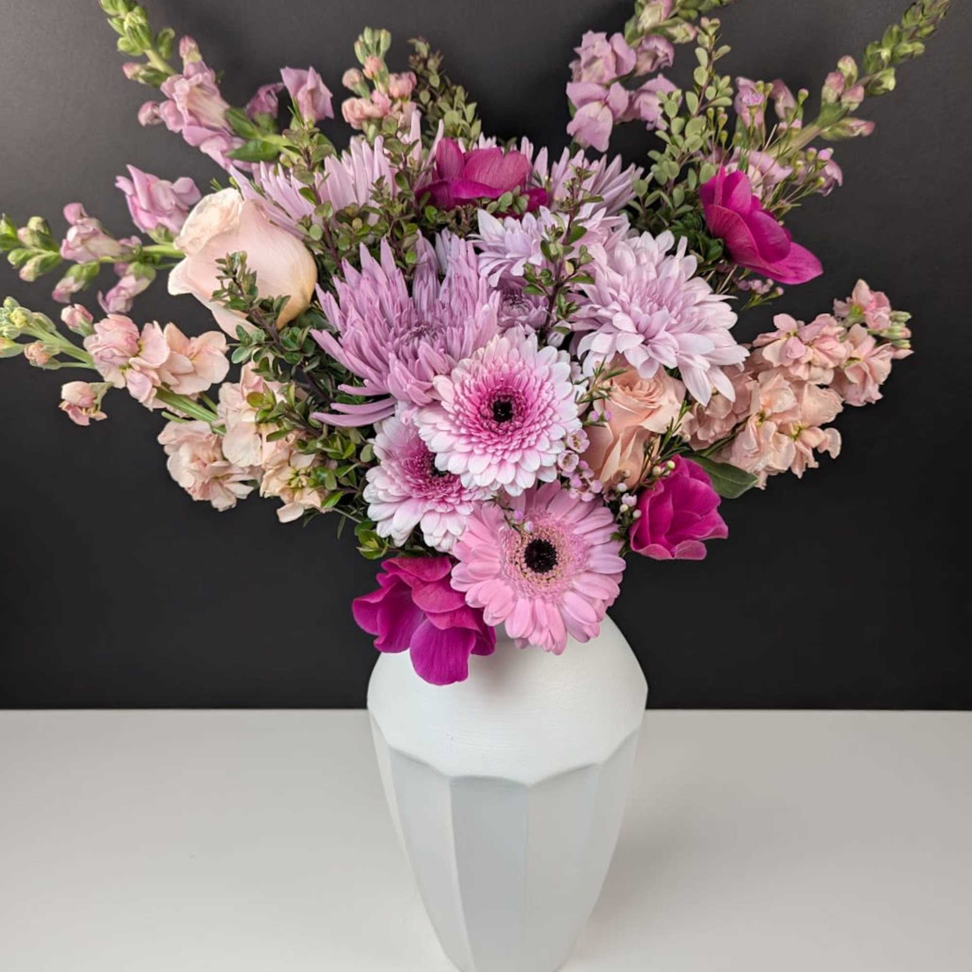Pink and lavender flowers arranged in a white vase