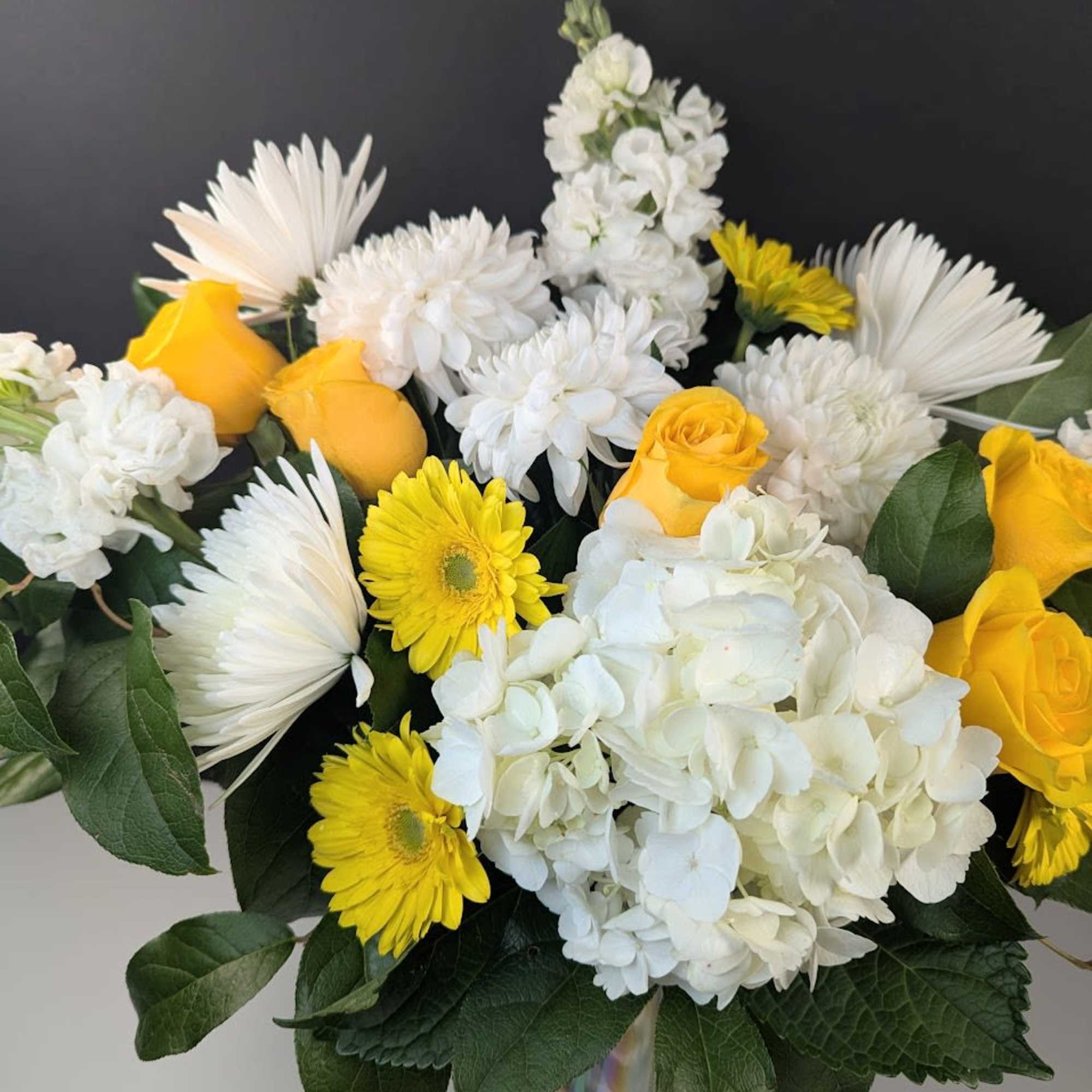 Bouquet of yellow roses, white hydrangeas, and white daisies in a glass vase