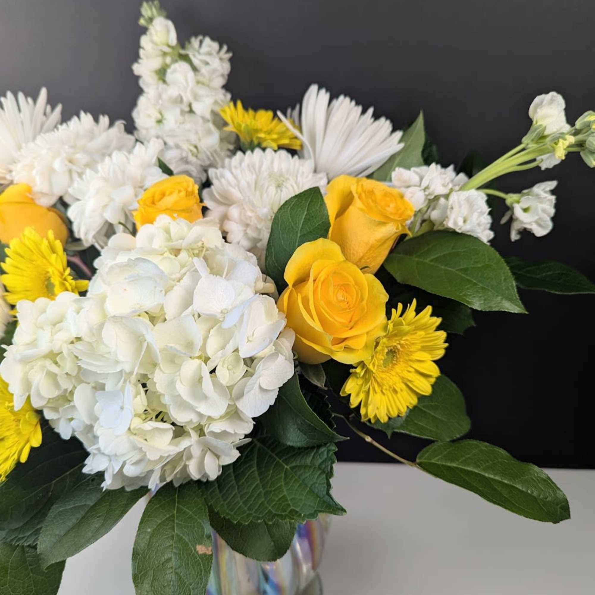 Yellow roses and white flowers arranged in a glass vase