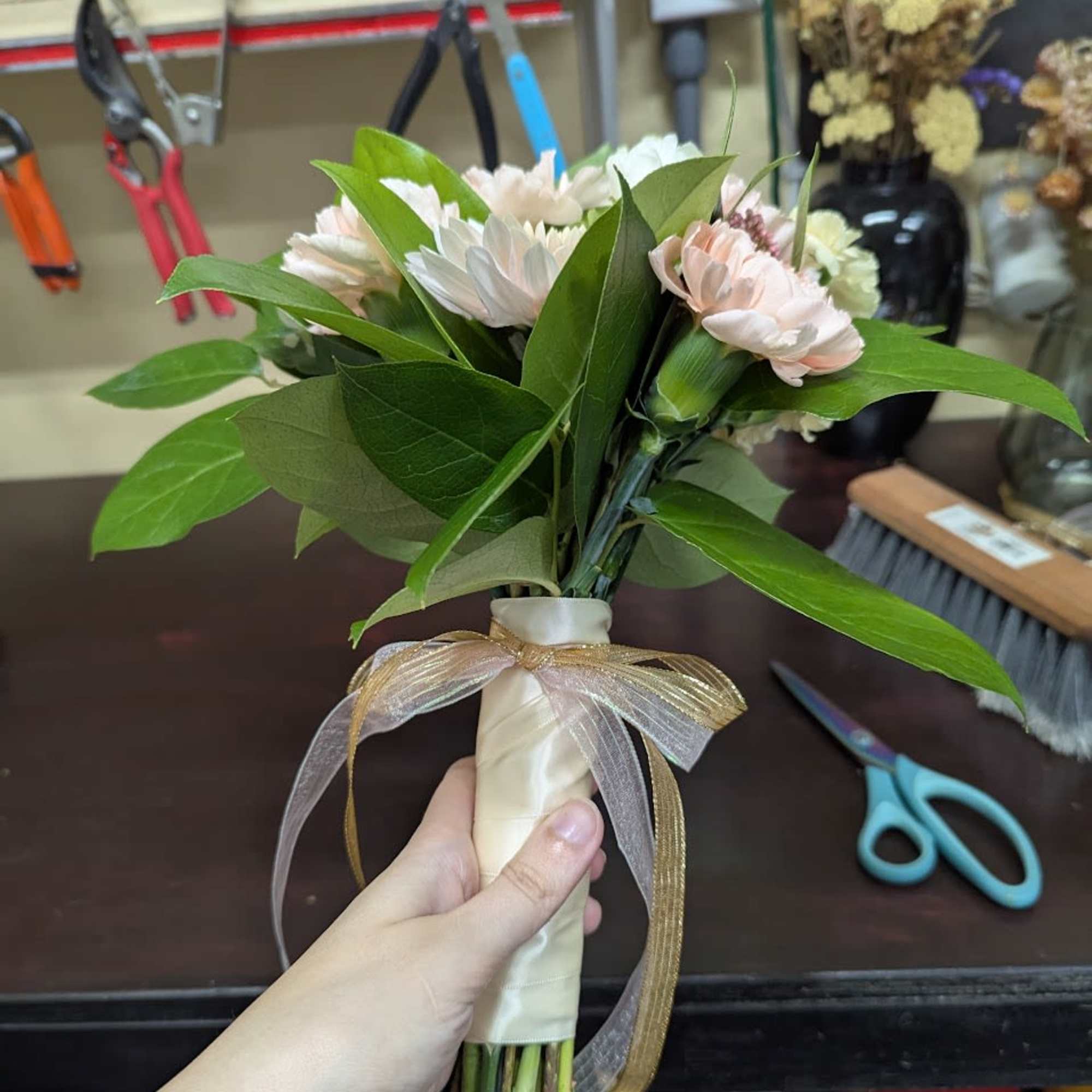 Handheld bouquet of pale pink and white flowers tied with a ribbon