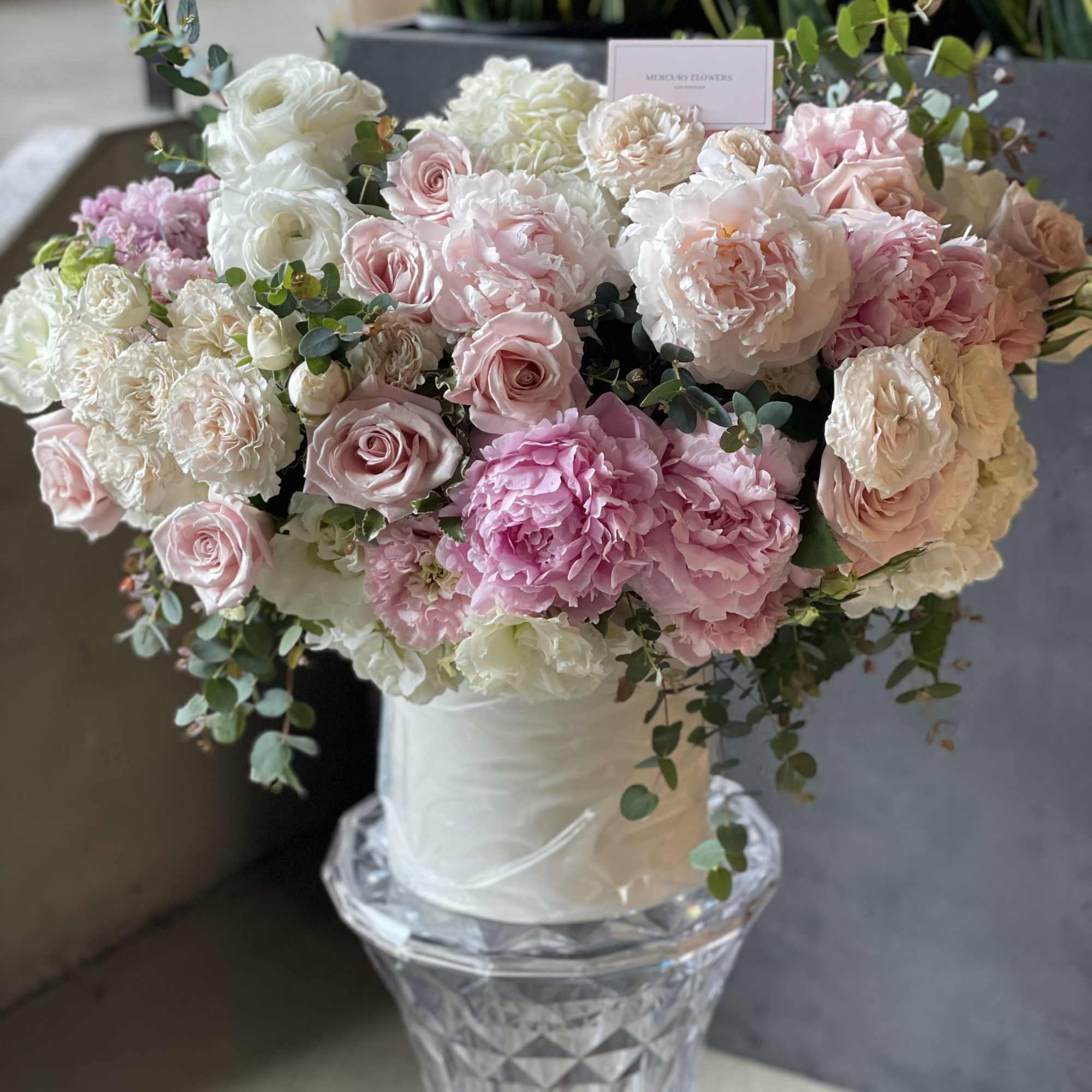 Pink and white rose bouquet in a white hat box on a glass pedestal