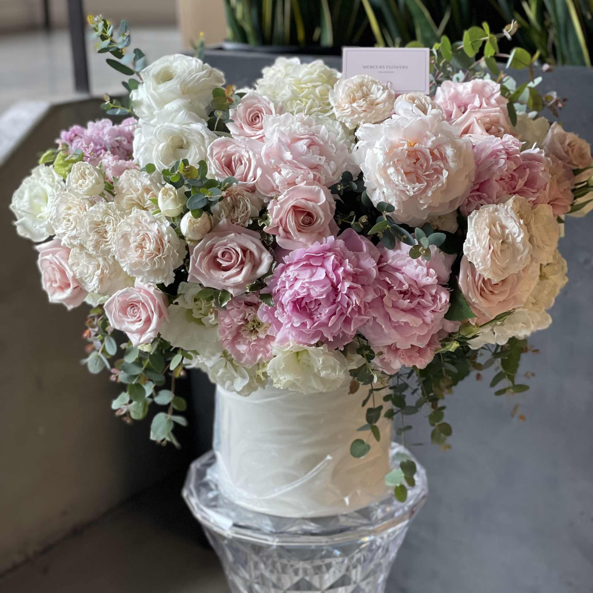 Large pink and white floral arrangement in a clear pedestal vase