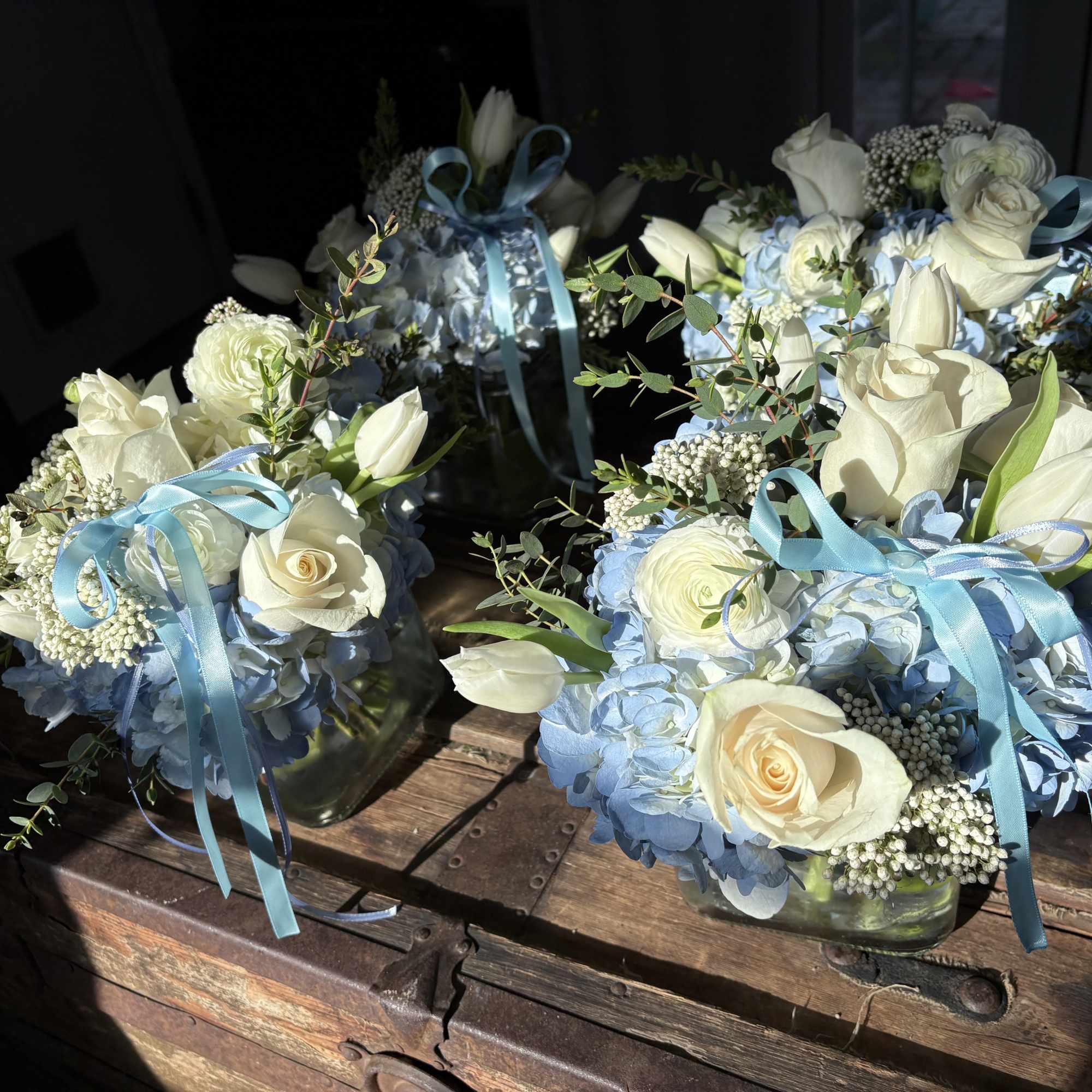 Blue and white floral arrangements in glass vases with ribbon bows
