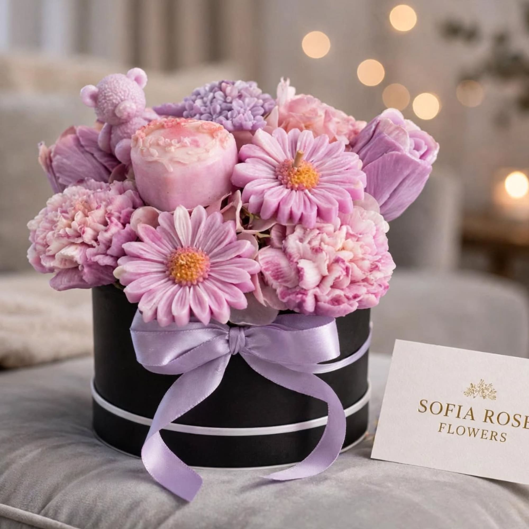 Pink and lavender flowers arranged in a black round box with a satin ribbon