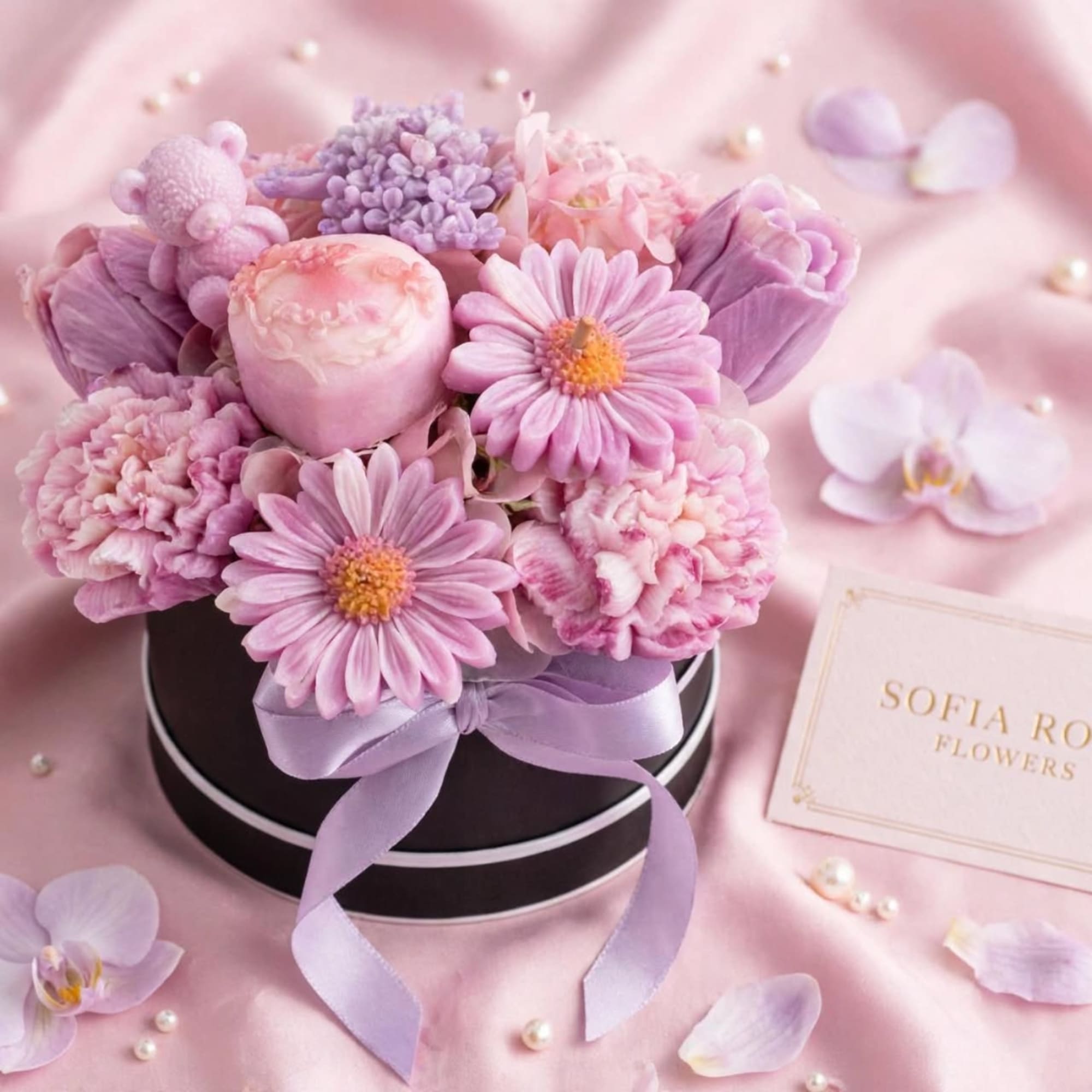 Pink and lavender flower arrangement in a black hat box with a ribbon