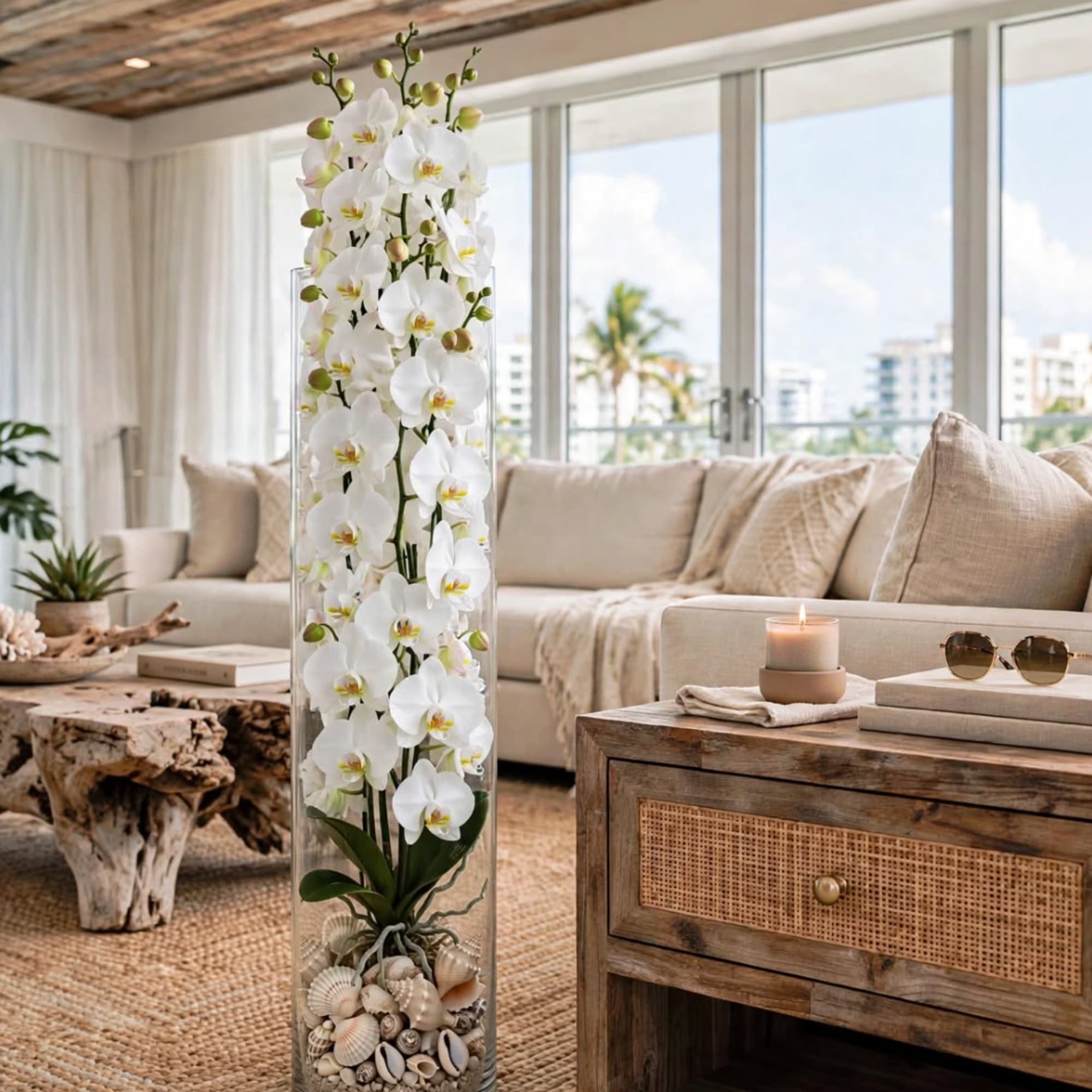 Tall white orchid arrangement in a clear glass vase with shells at the base