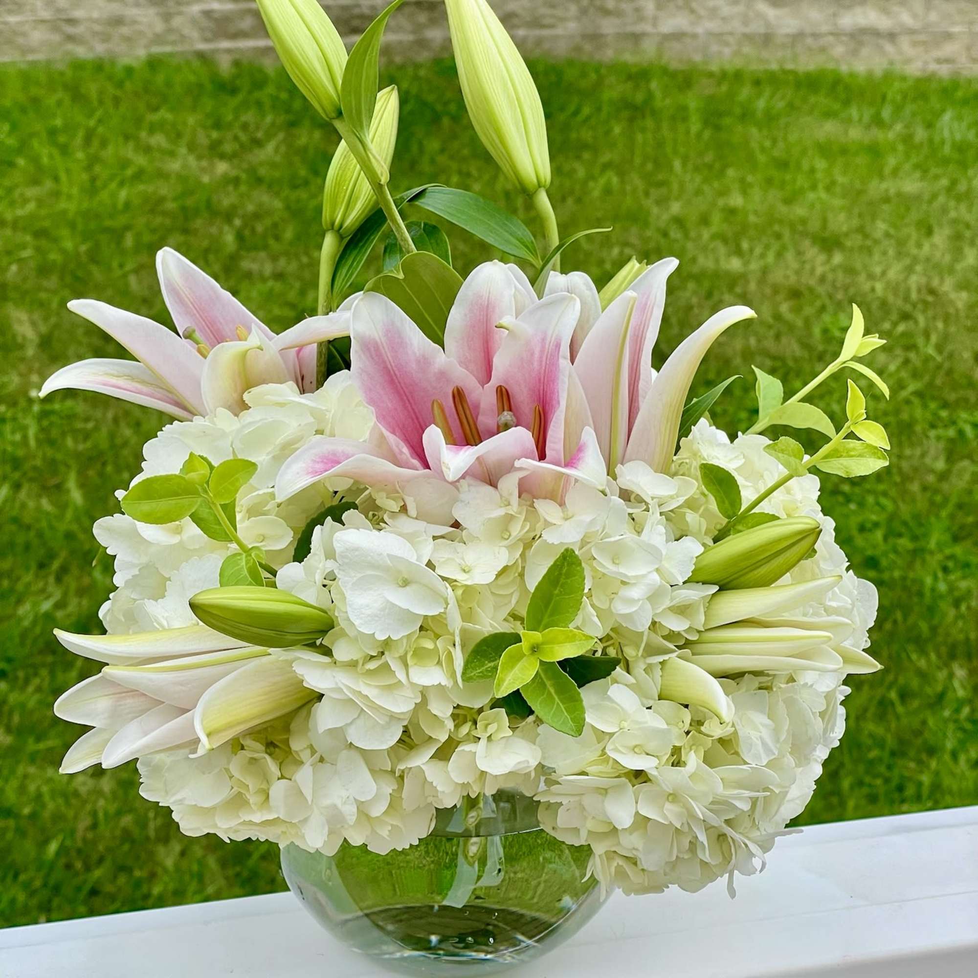 Pink and white lilies arranged in a clear glass vase with white hydrangeas